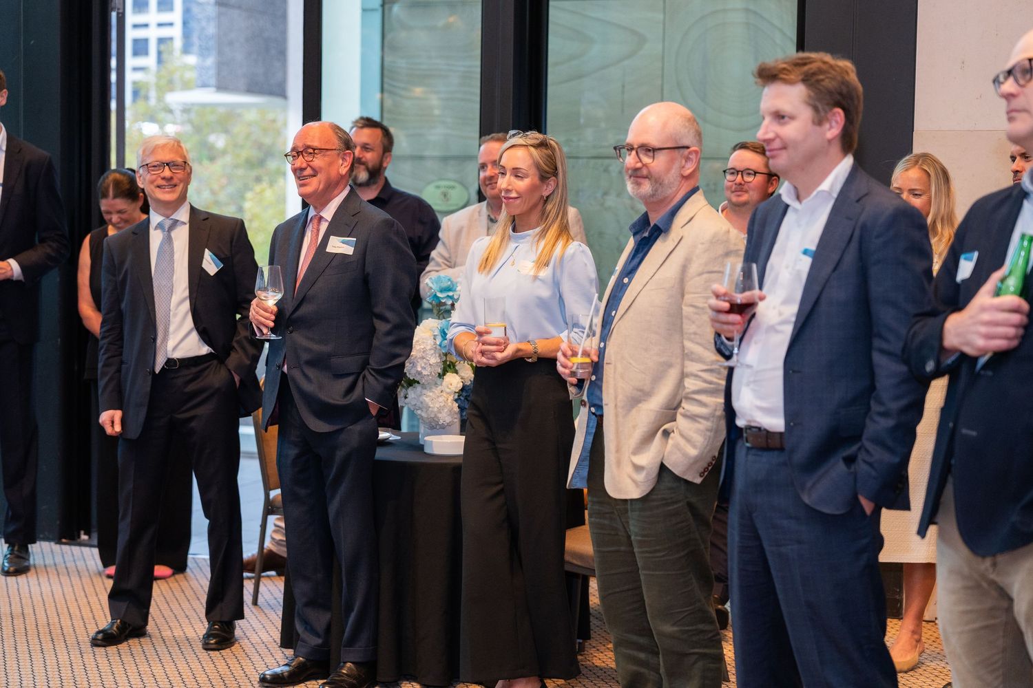 Group of professionals networking at a corporate event, holding drinks and engaging in conversation in a modern venue.