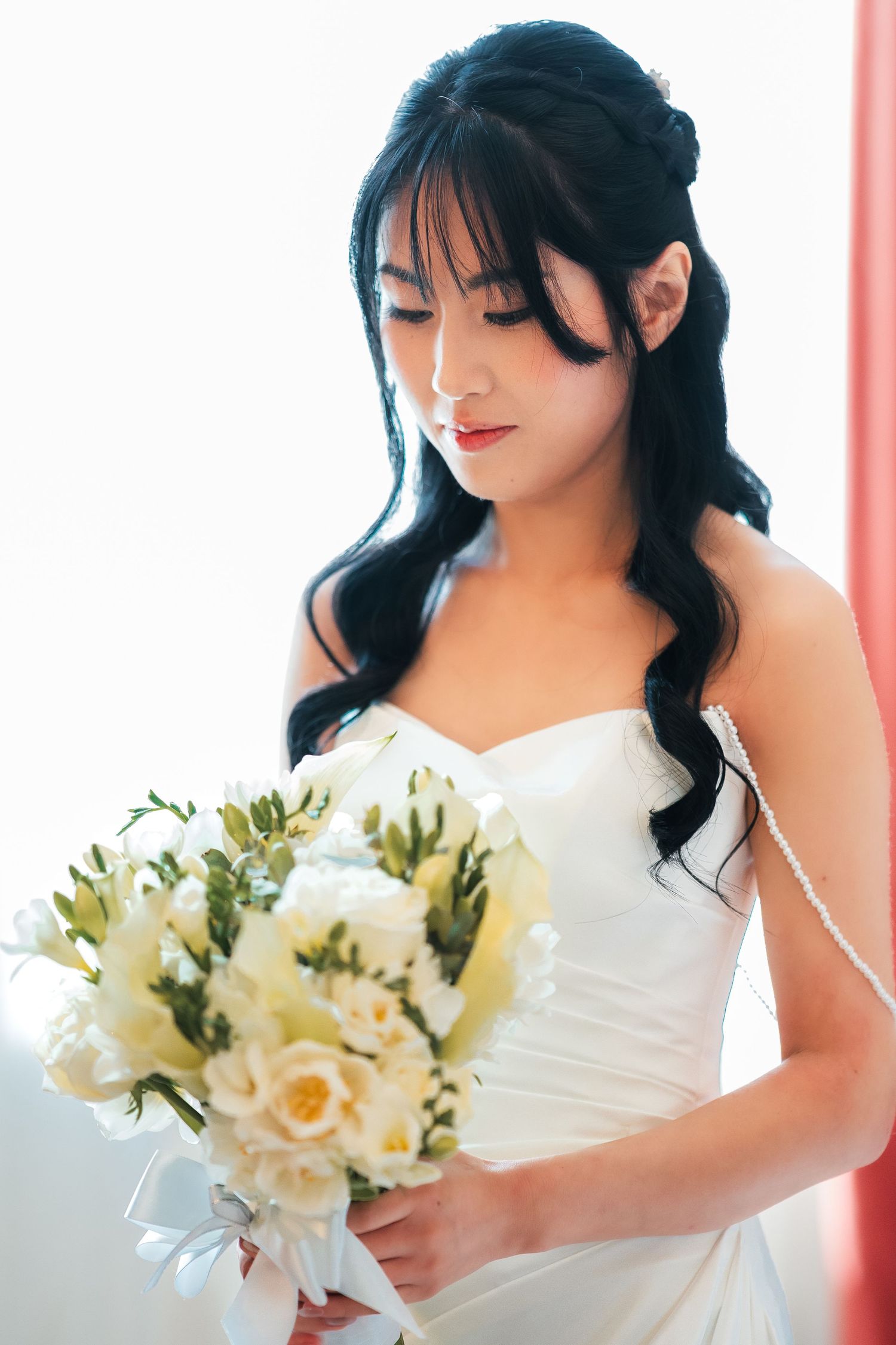 Beautiful Asian bride in a strapless white gown holding an elegant bouquet of white roses.