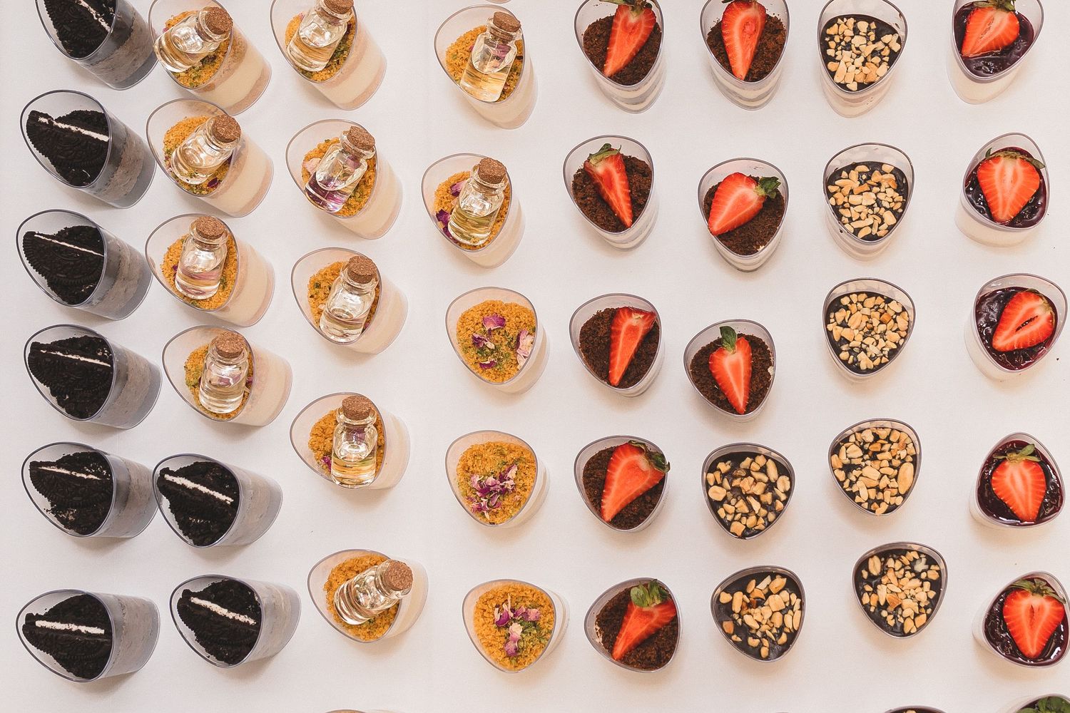 Overhead view of elegant dessert cups with chocolate, strawberries, and nuts on white surface.
