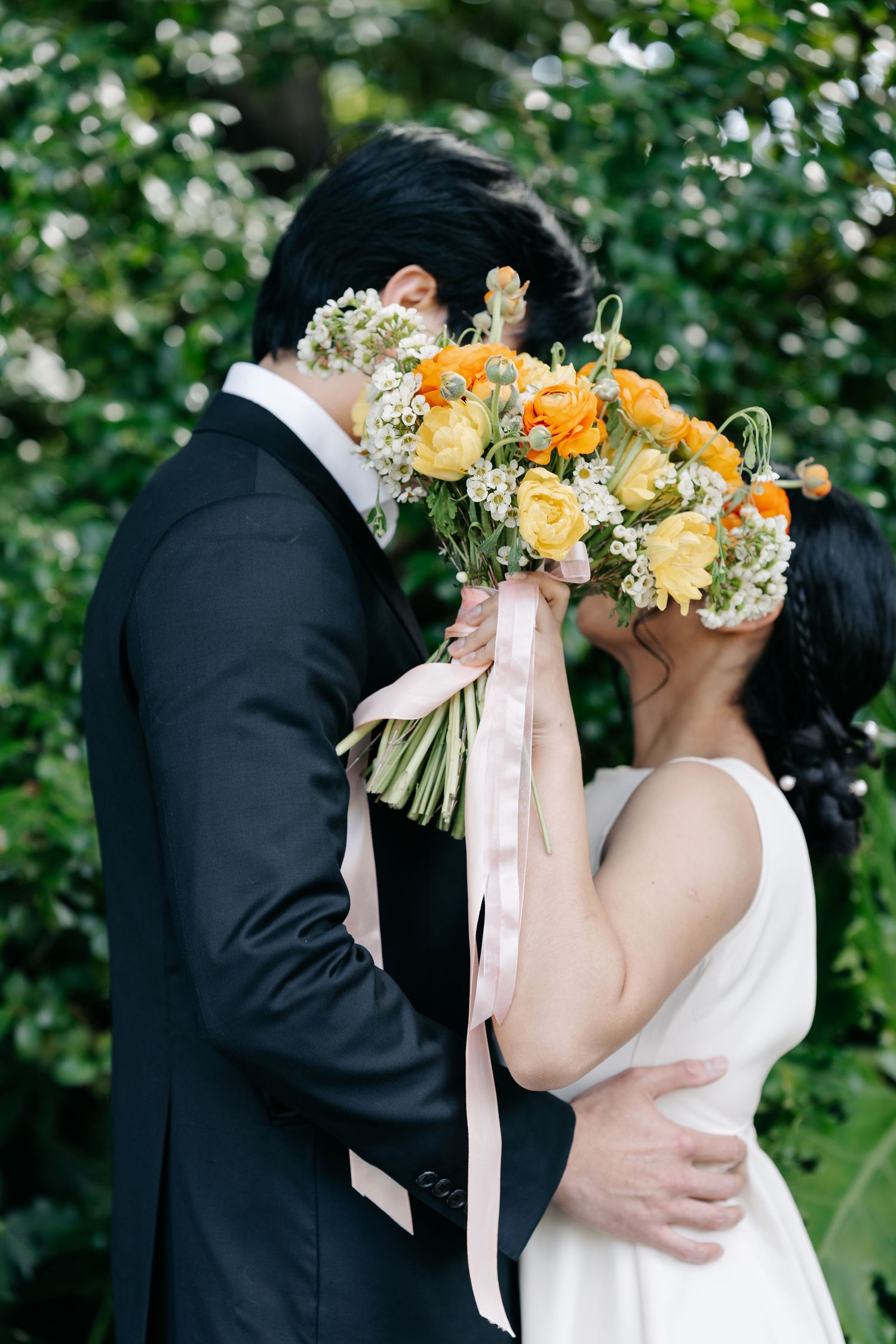 A couple shares an intimate moment behind a beautiful bouquet of yellow and orange flowers.