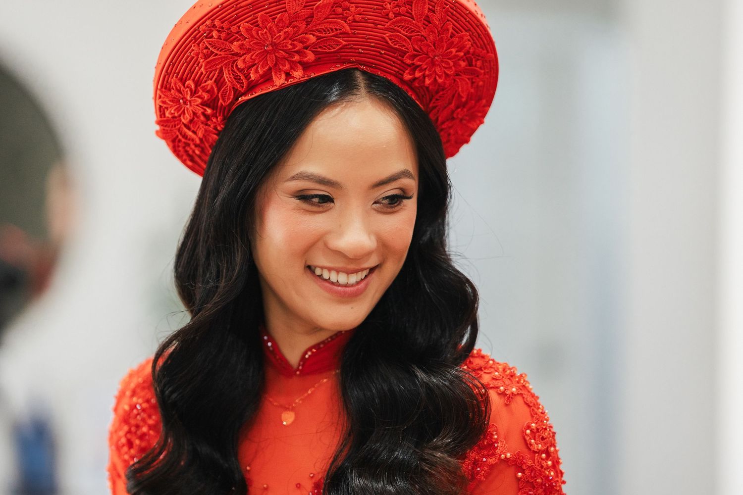 Young Vietnamese woman smiling in traditional red ao dai dress and non la hat, elegant bridal attire.