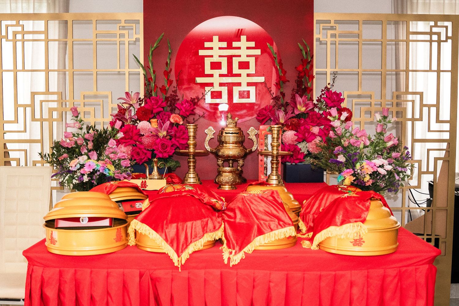 Traditional Chinese wedding altar with double happiness symbol, red decor, gold ornaments, and floral arrangements.