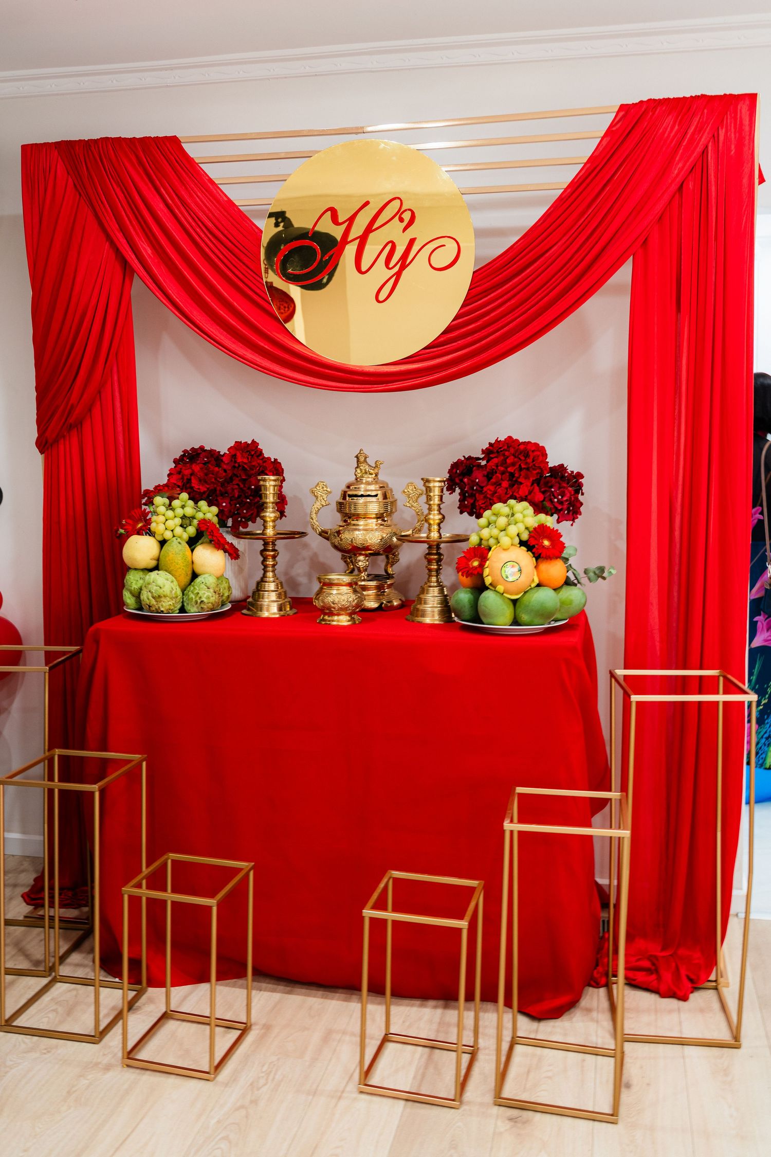 Elegant Vietnamese wedding altar with red draping, gold samovar, tropical fruits, and floral arrangements on a decorated table.