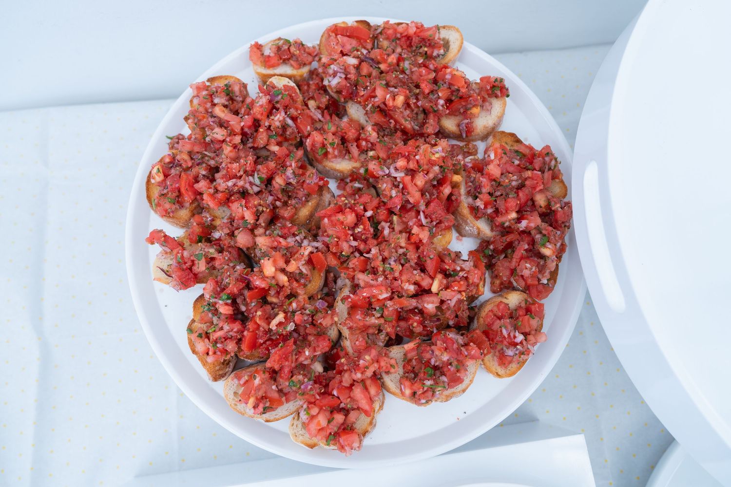 White plate of bruschetta topped with diced tomatoes, herbs, and olive oil on toasted bread slices.