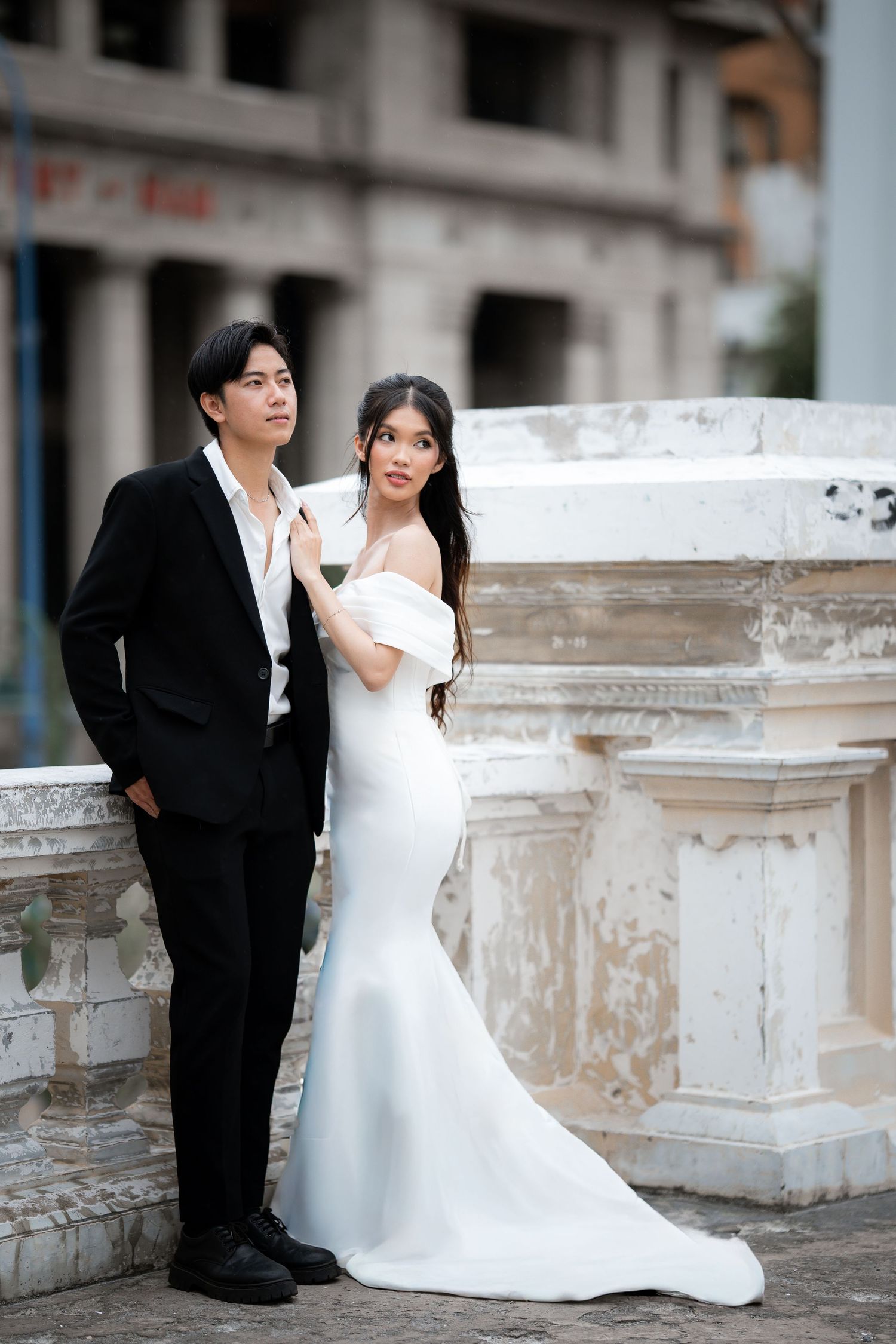 Wedding couple poses by weathered stone balustrade during outdoor photo session.