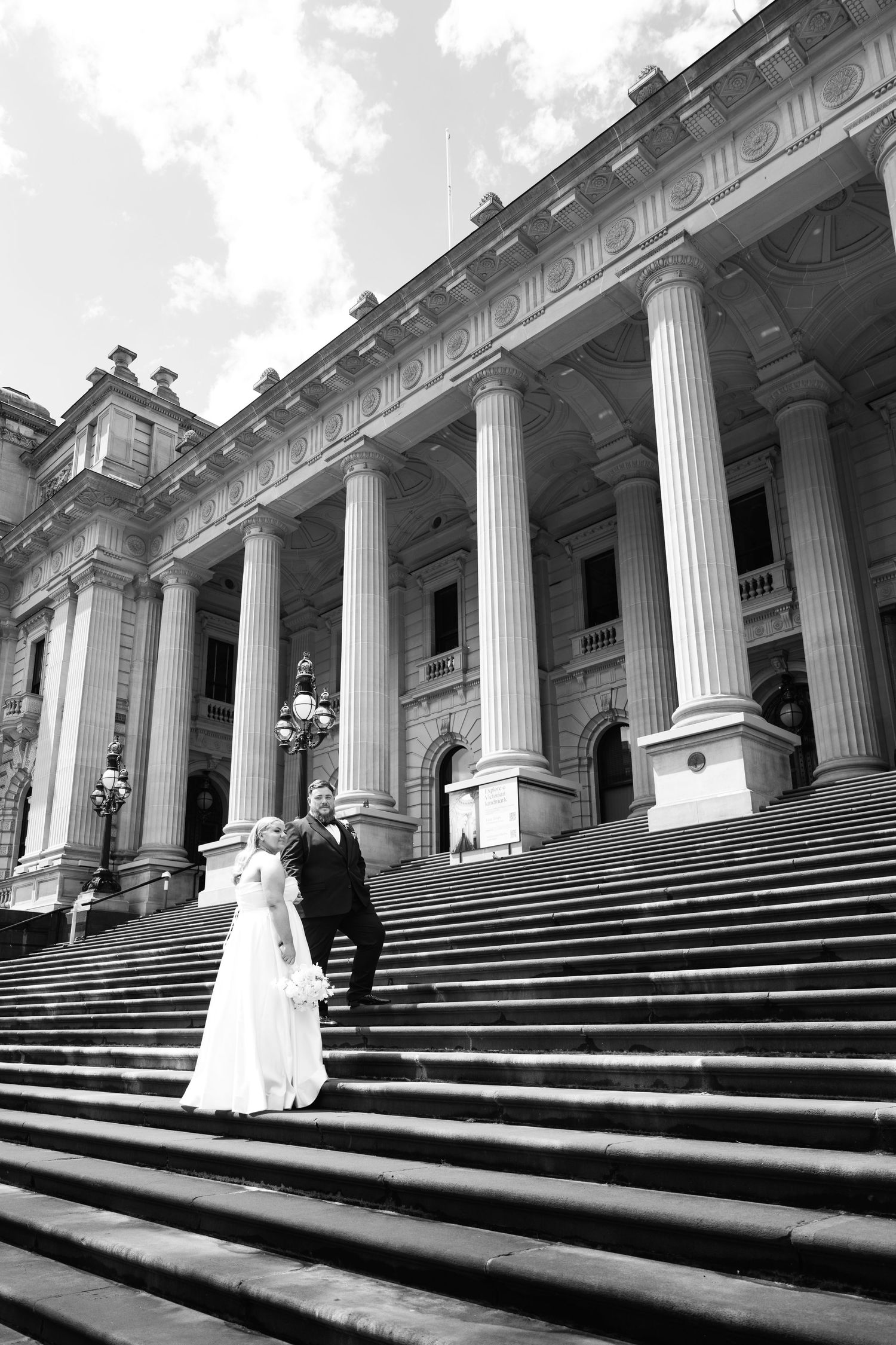 Black and white photo of a bride and groom posing on grand steps of a classical columned building.