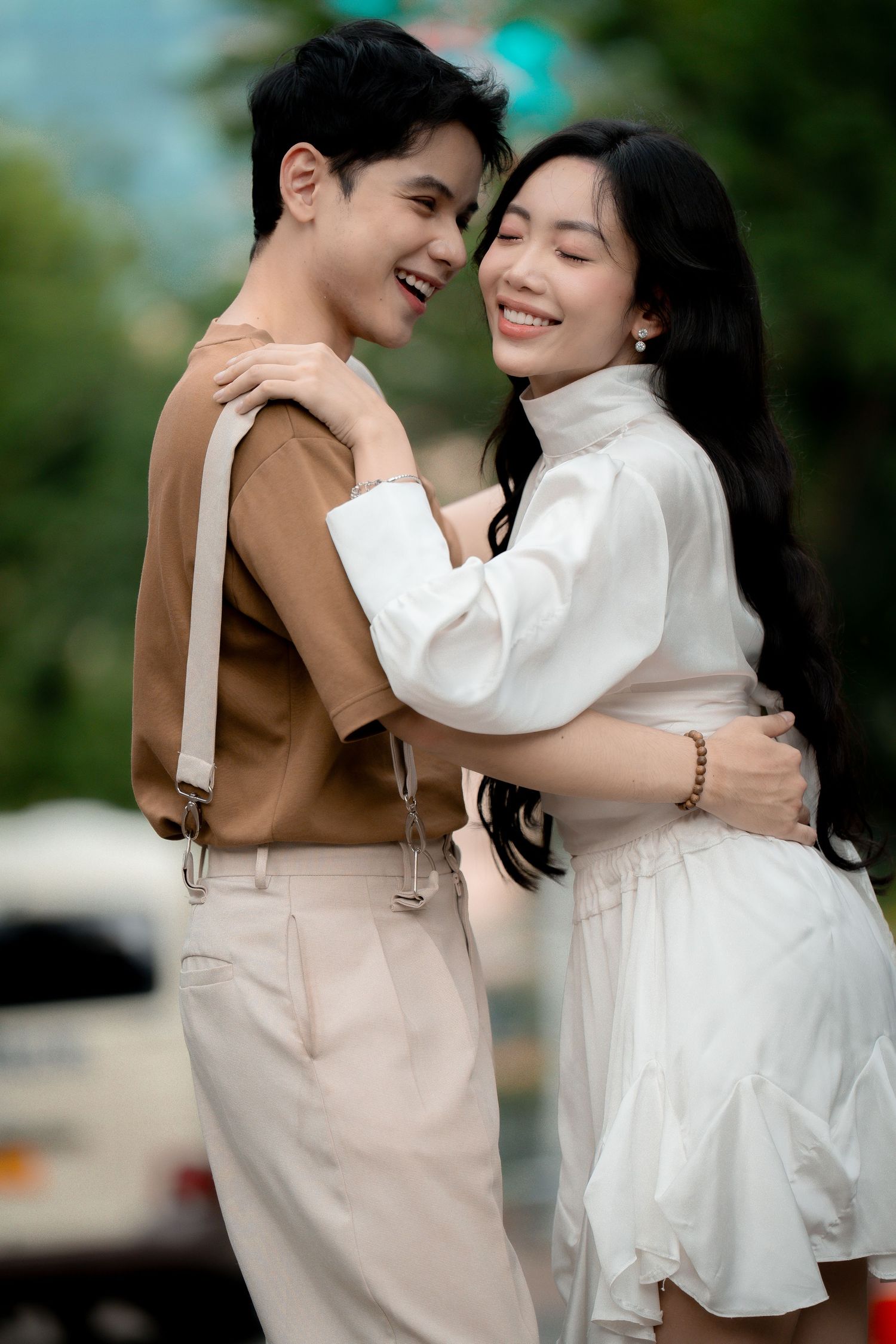 A couple in contrasting outfits of beige and white share joyful embraces outdoors.