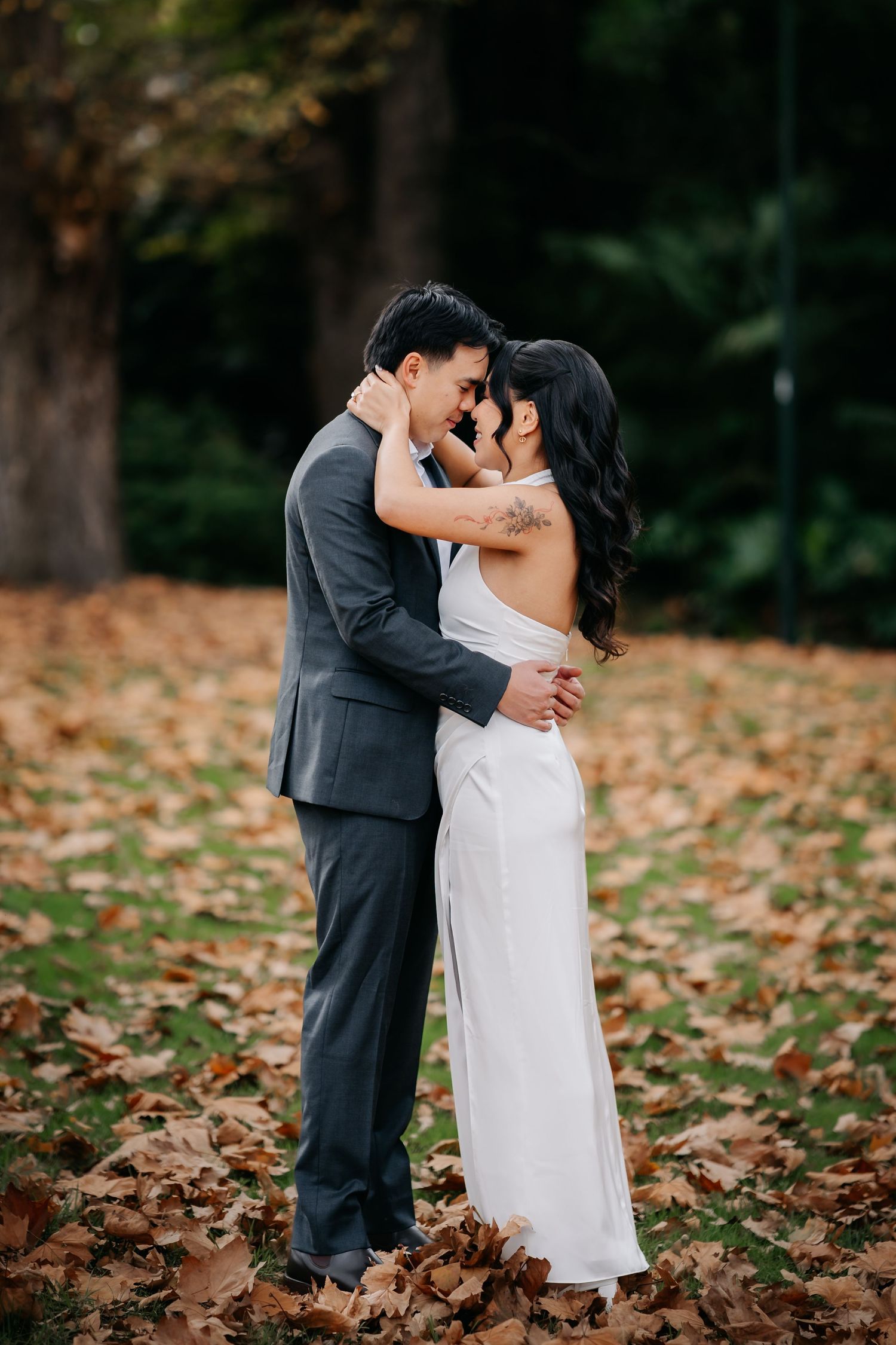 Bride and groom sharing a romantic forehead touch moment surrounded by fallen autumn leaves.