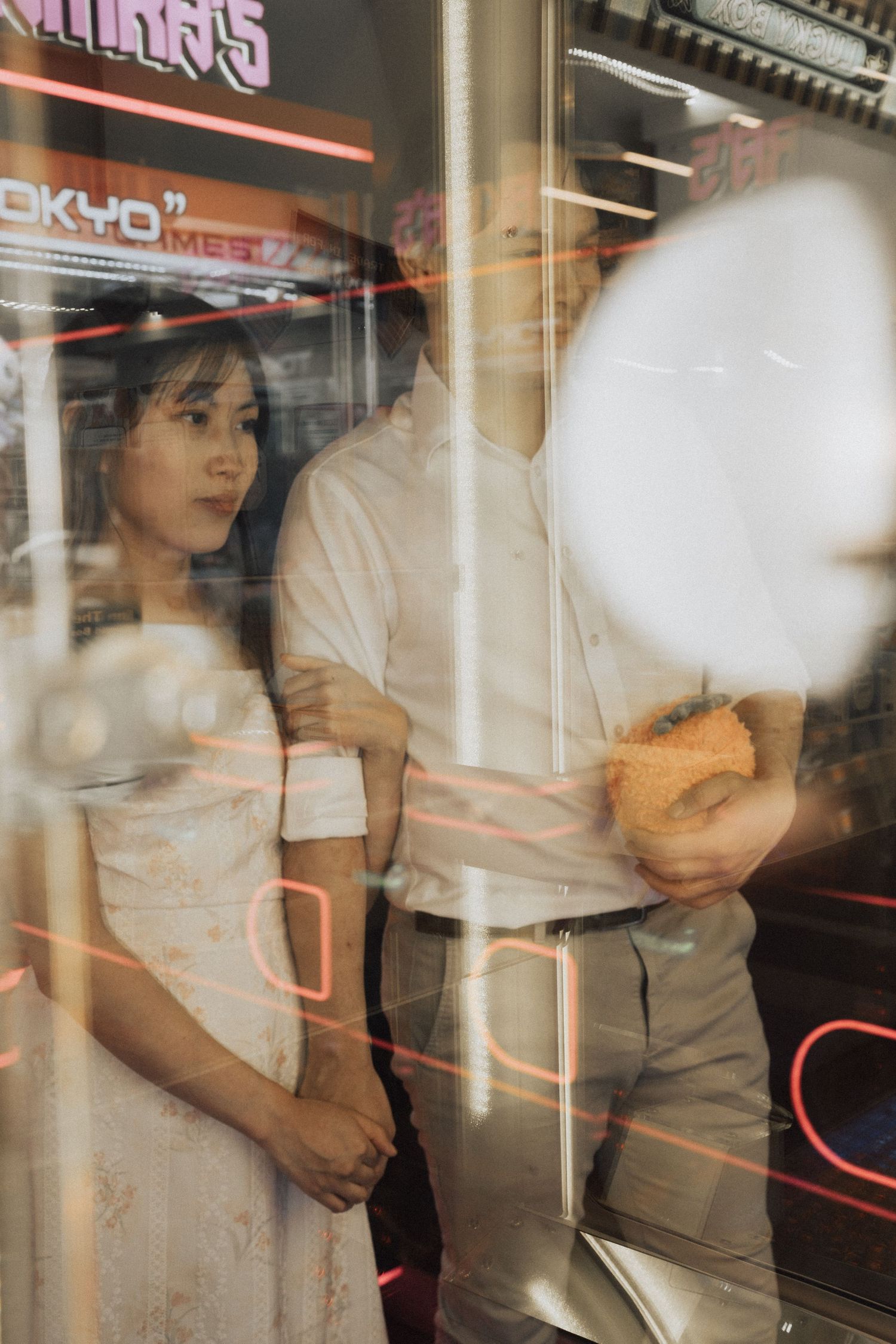 Couple standing together behind glass with neon reflections in urban setting.