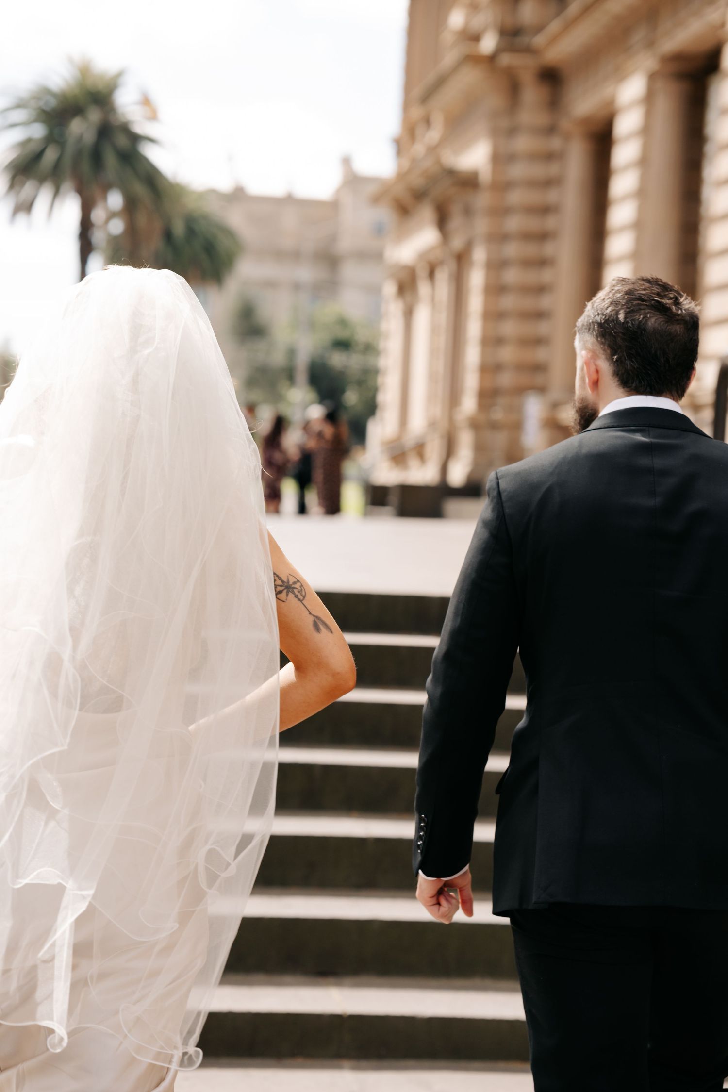 Romantic wedding couple walking along classic architectural columns and palm trees.