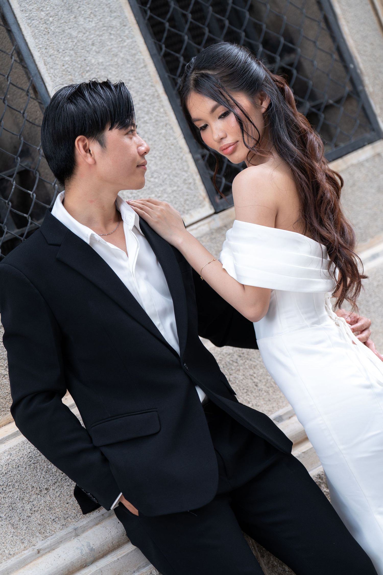 A couple in formal wedding attire poses together against a stone wall in an artistic series of shots.