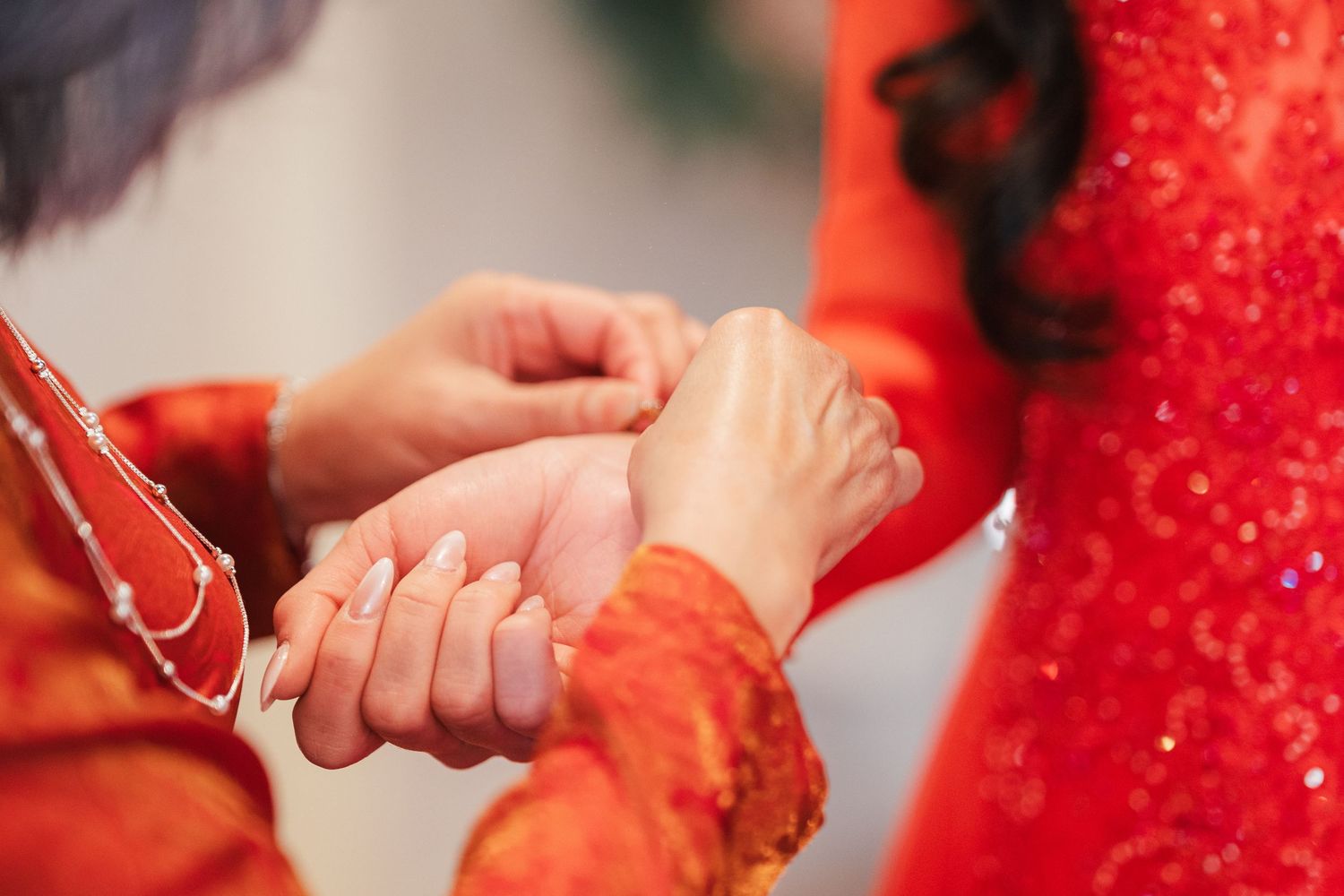 Close-up of hands exchanging bracelet jewelry during Vietnamese traditional wedding ceremony.