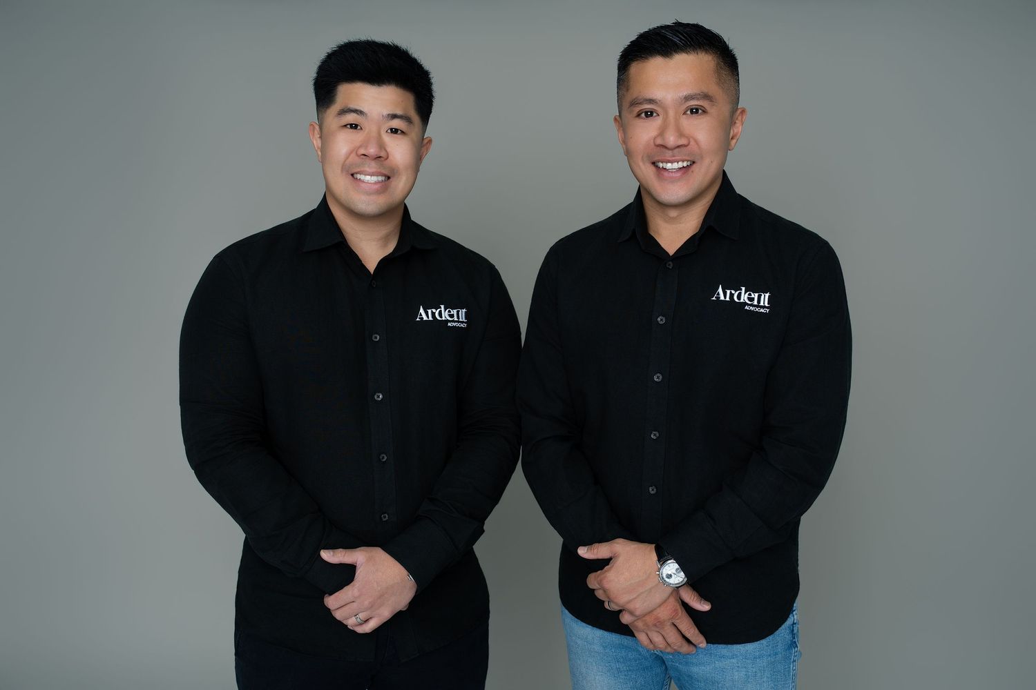 Two smiling men in matching black Ardent branded shirts pose together against a gray background.