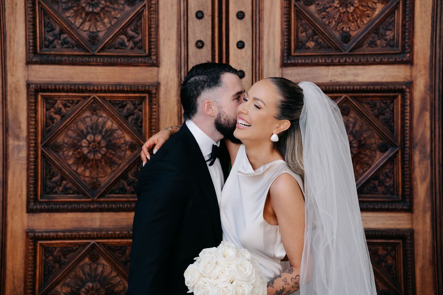 Intimate wedding portrait against decorative wooden panels with bride holding white bouquet.