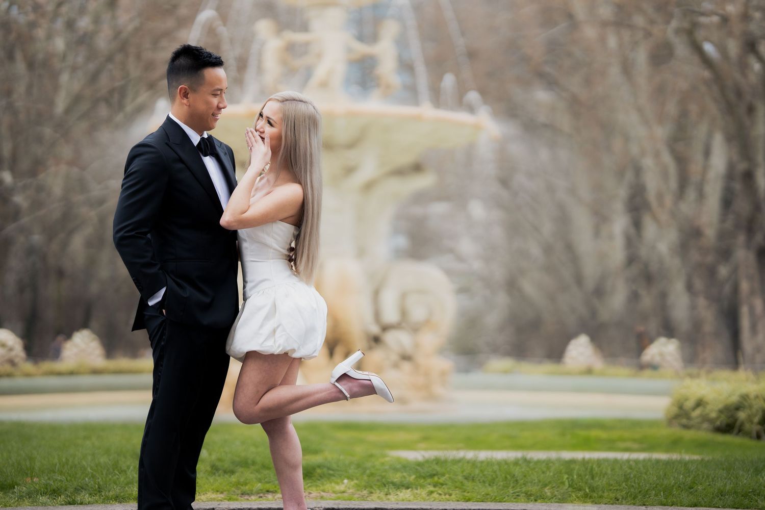 A playful engagement photo with the bride lifting her leg while embracing outdoors.