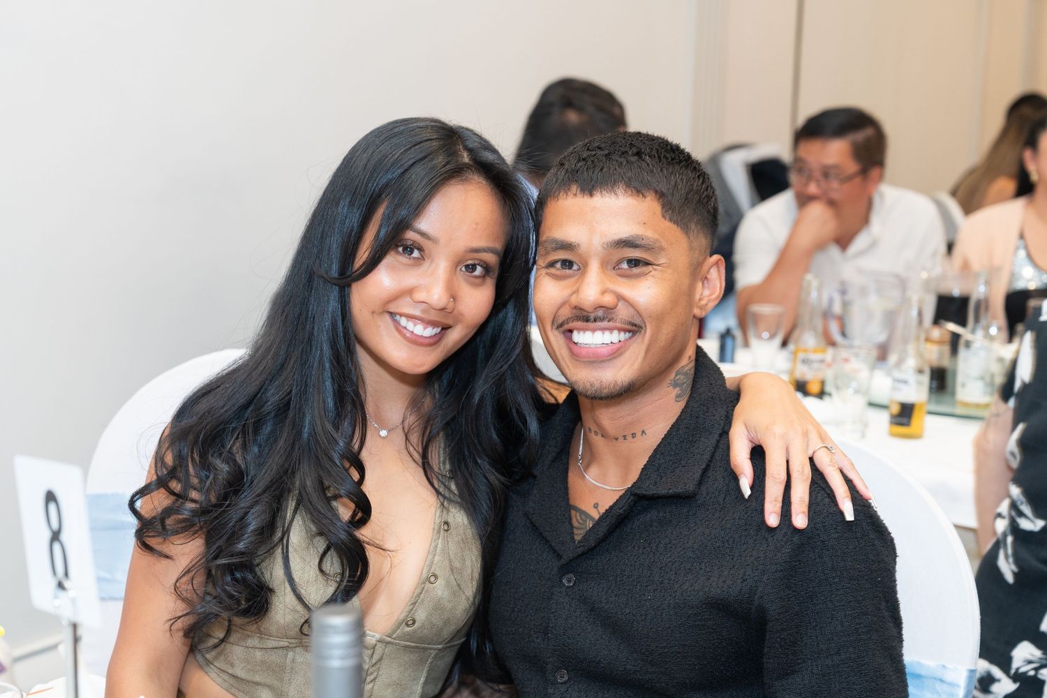 Smiling couple posing together at a formal dinner event, woman in gold dress and man in black shirt.