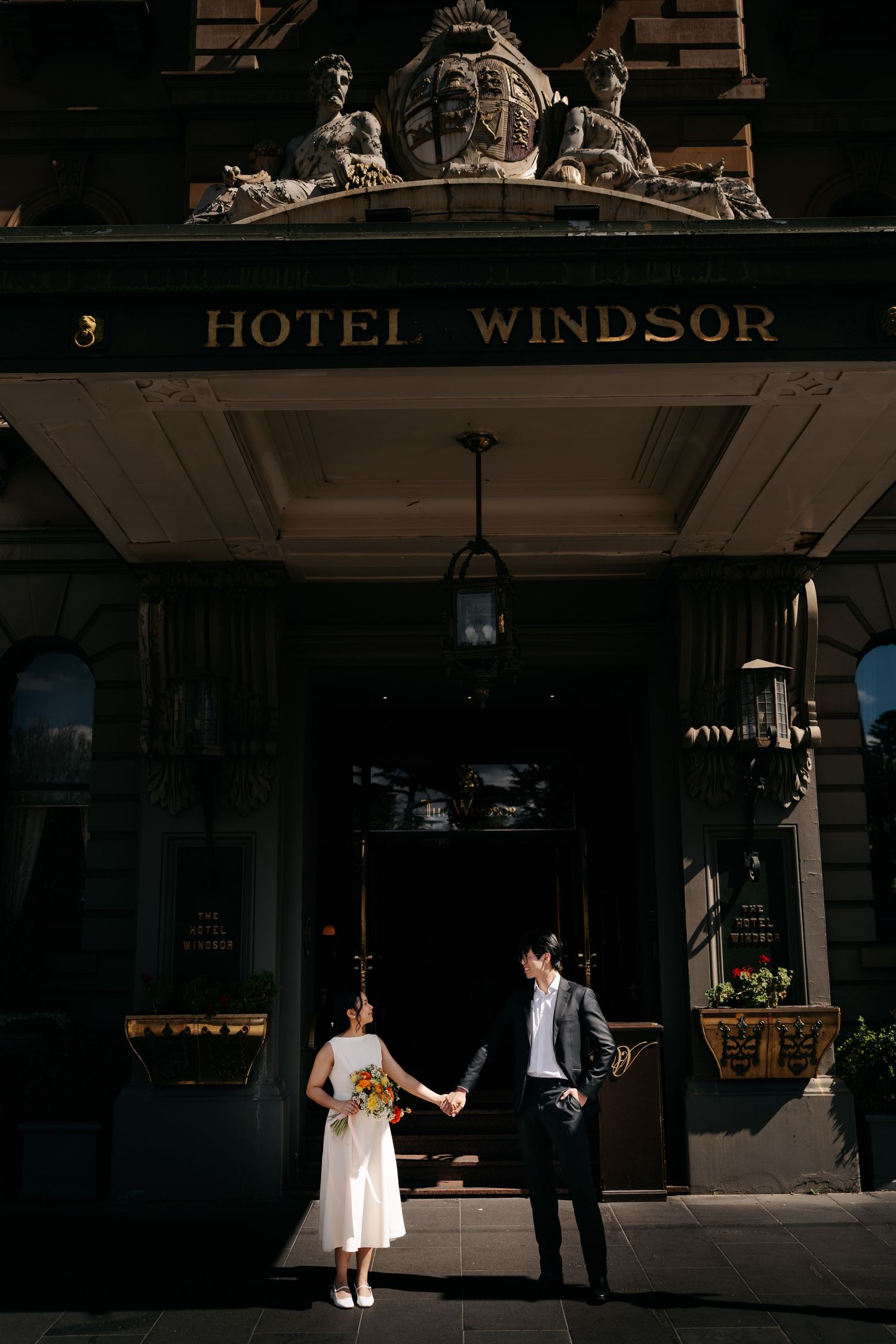 Dramatic shadows frame couple posing outside historic Hotel Windsor entrance.