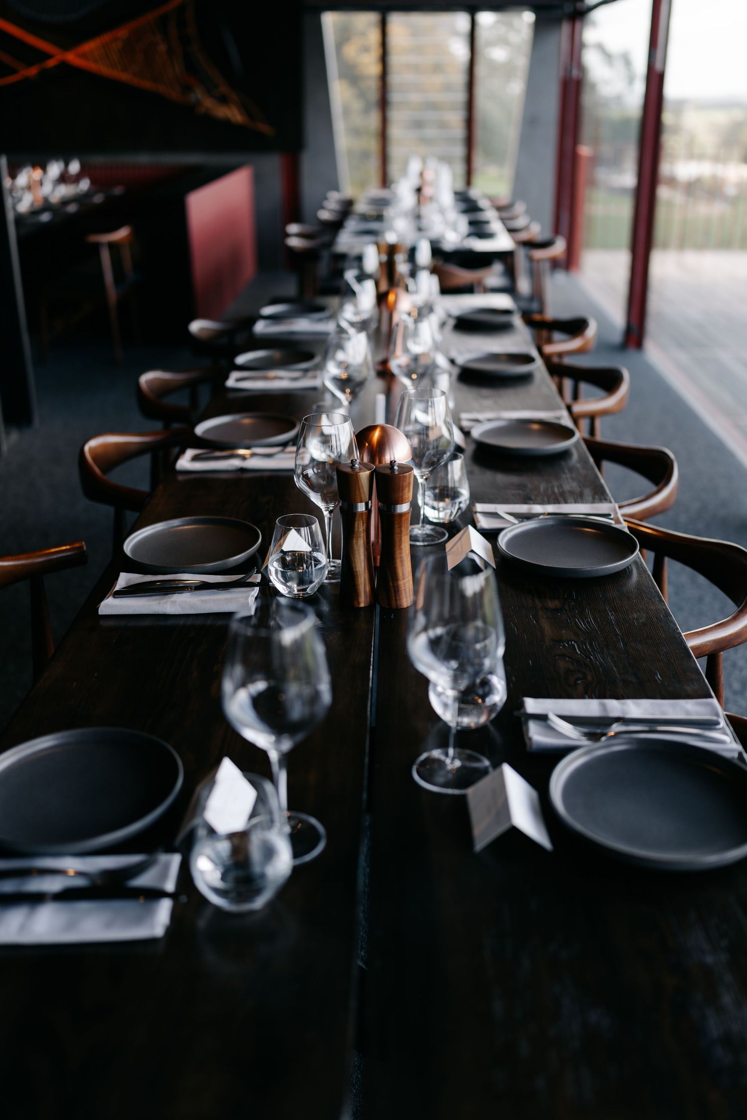 Elegant table settings with dark plates and glassware arranged in a modern restaurant interior.