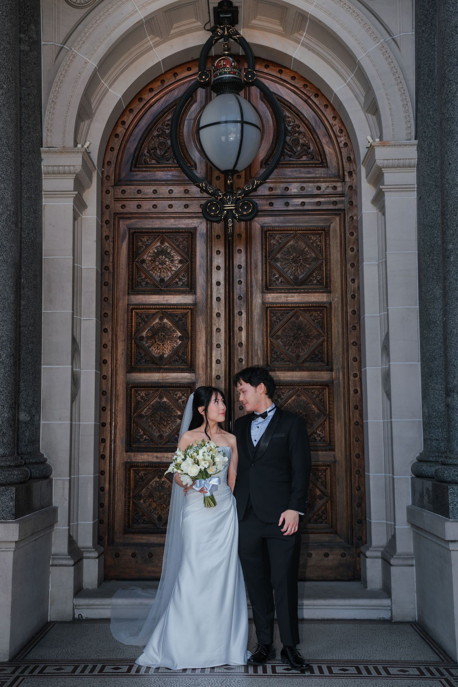 Bride and groom standing together under an ornate arched doorway with a decorative lantern.
