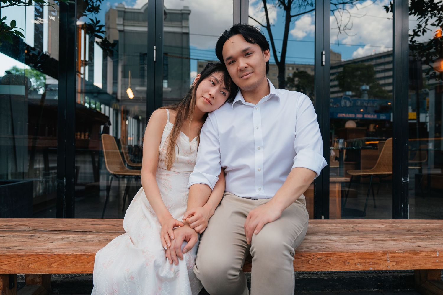 Couple sitting closely on wooden bench outdoors, woman leaning on mans shoulder.