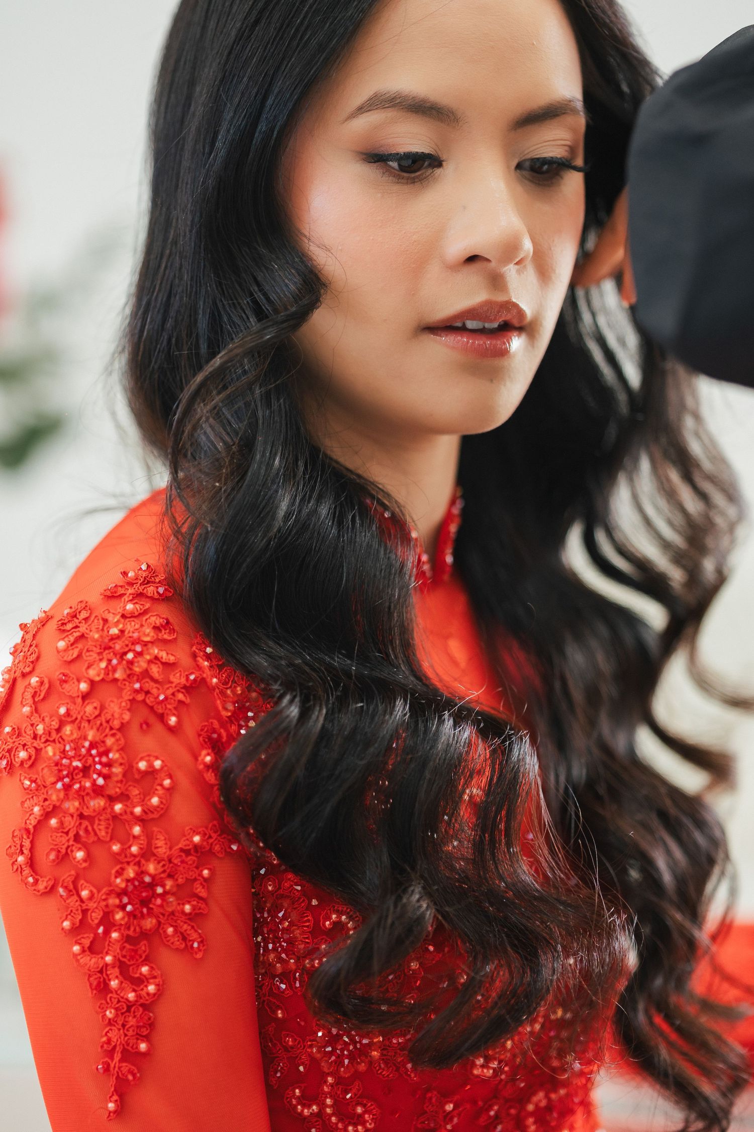 Beautiful Vietnamese bride in ornate red ao dai with beaded embroidery and flowing black wavy hair at traditional wedding.