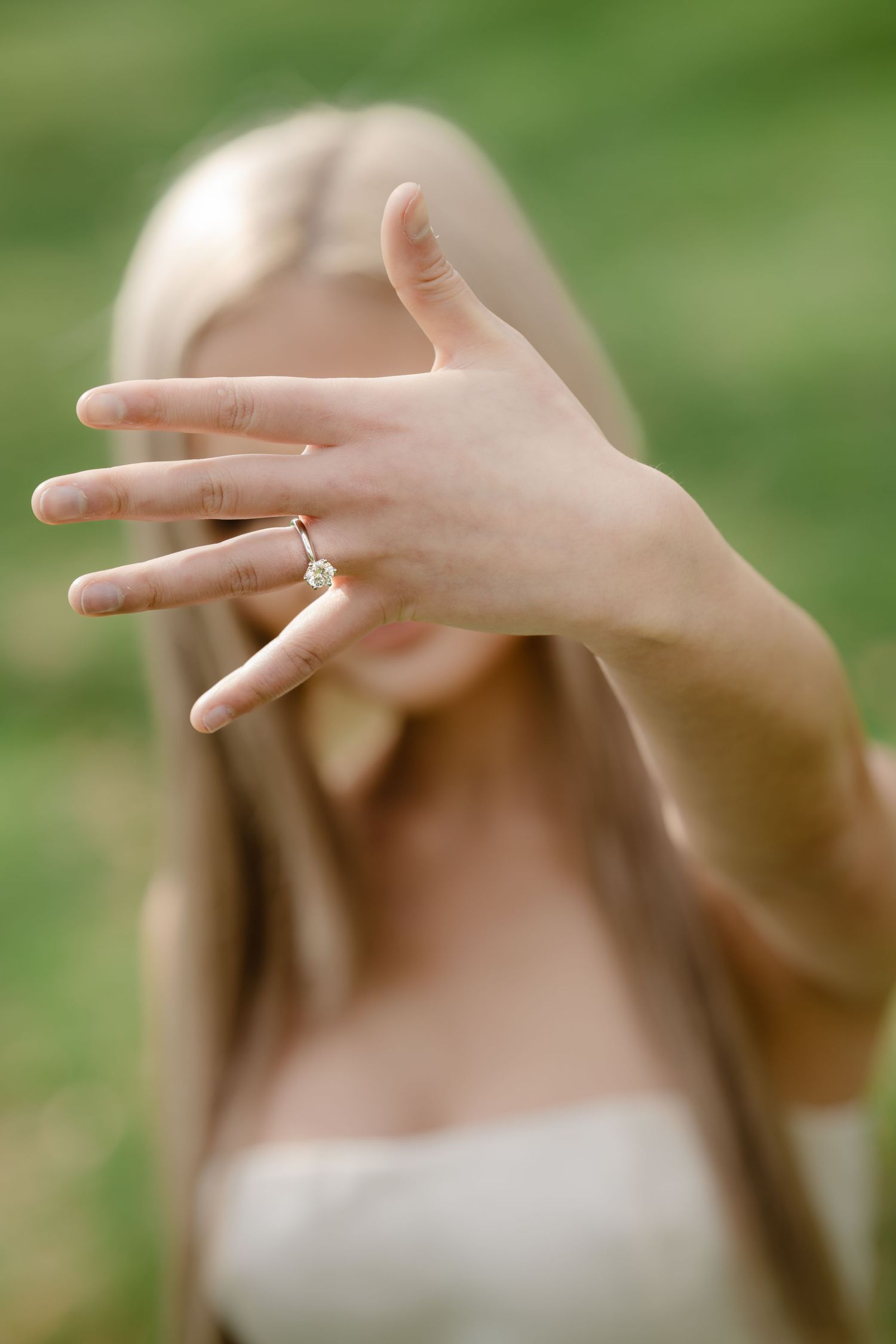 Close-up of hands displaying an engagement ring against a blurred green background.