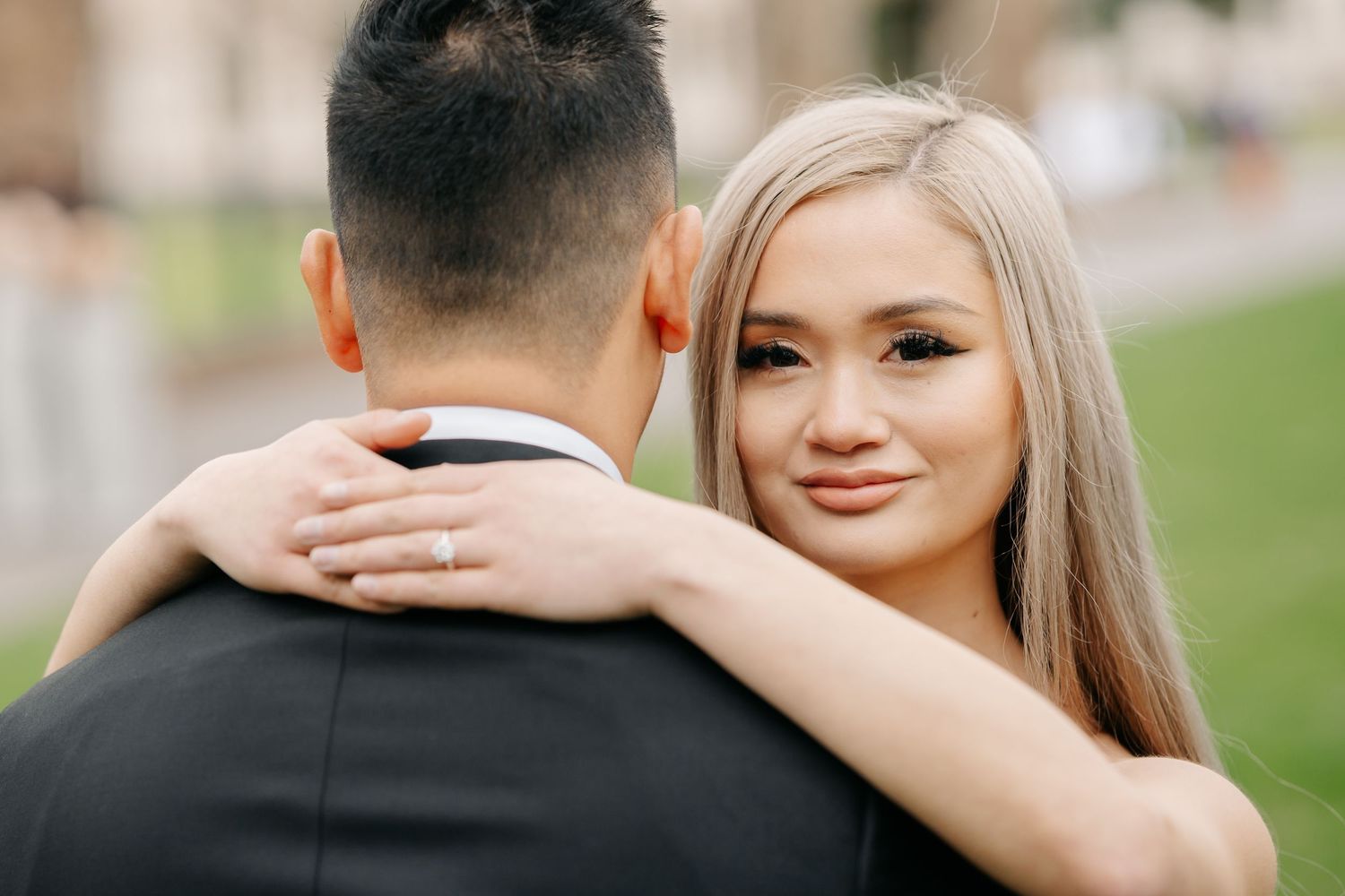 Close-up of couple embracing during wedding photoshoot on green lawn.