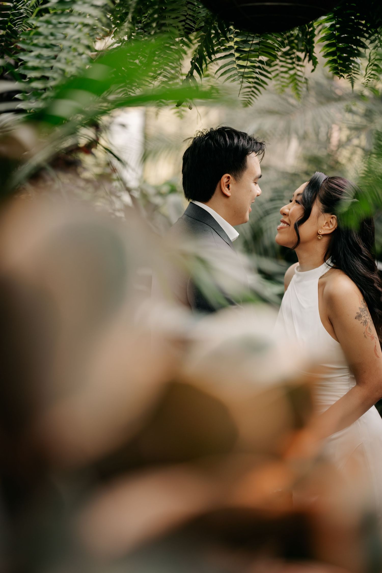 A couple shares a romantic moment surrounded by lush tropical ferns and greenery during their wedding day.