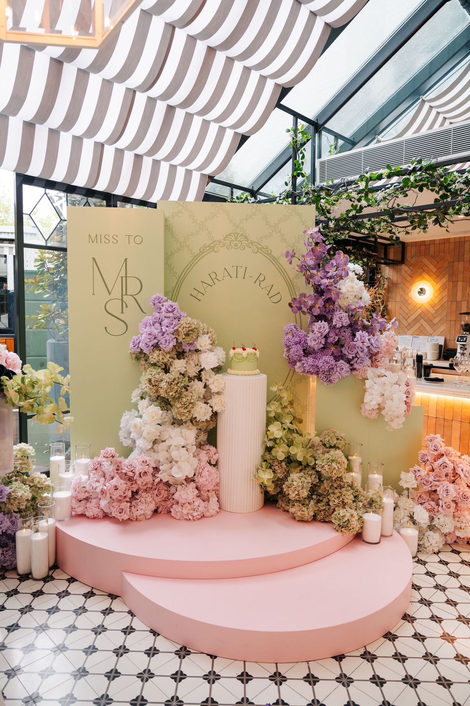 Elegant bridal shower display with pink floral arrangements, candles, and a cake on a pastel pink stage with Miss to Mrs signage.