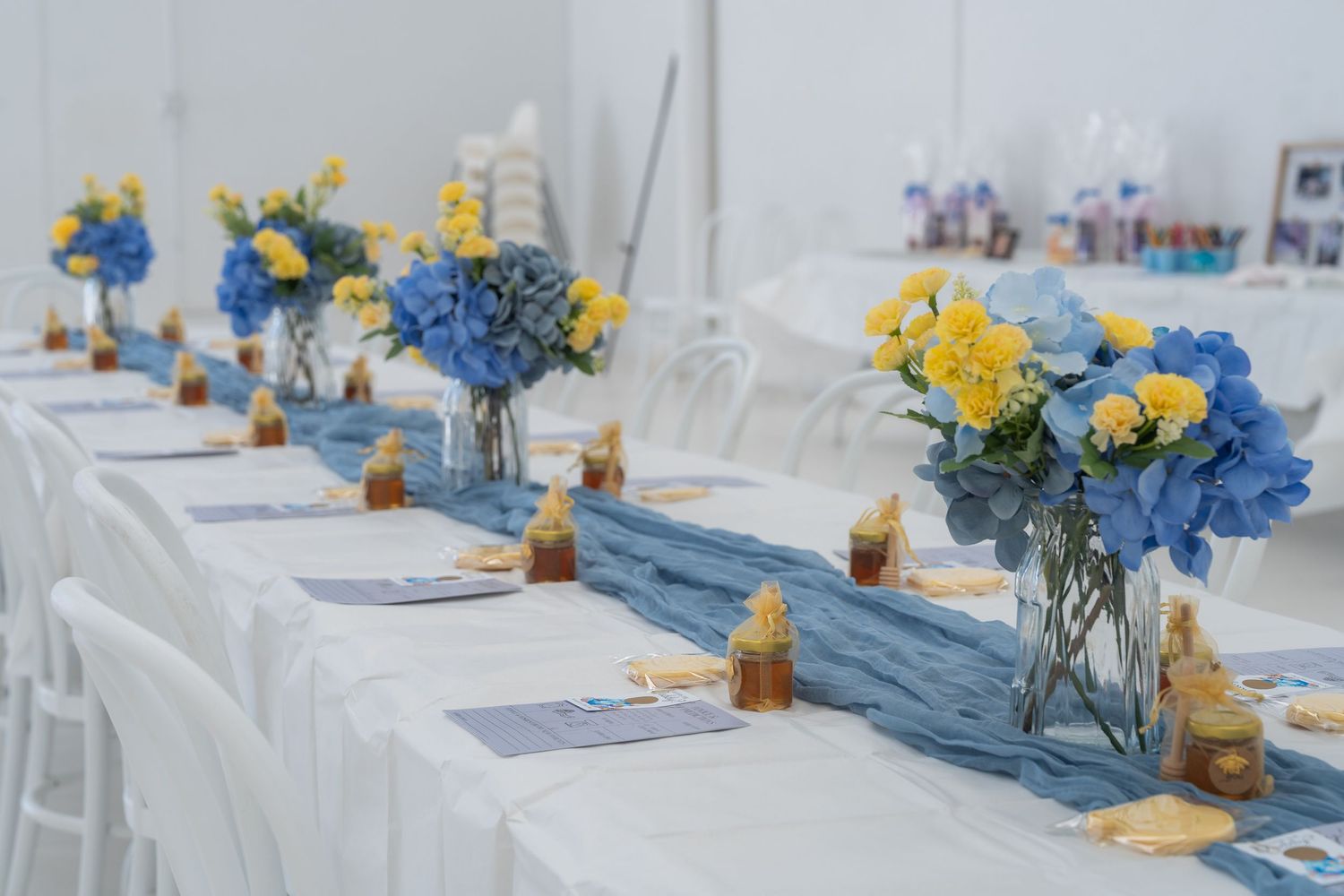 Elegant banquet table with blue hydrangea and yellow flower centerpieces on a white tablecloth with blue runner.