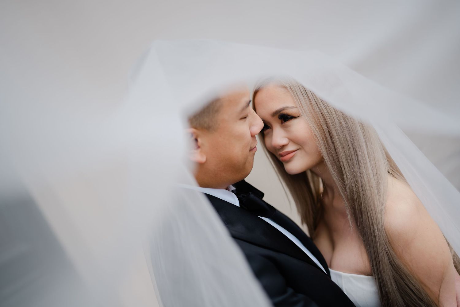 Romantic wedding portrait with flowing veil against soft light background.