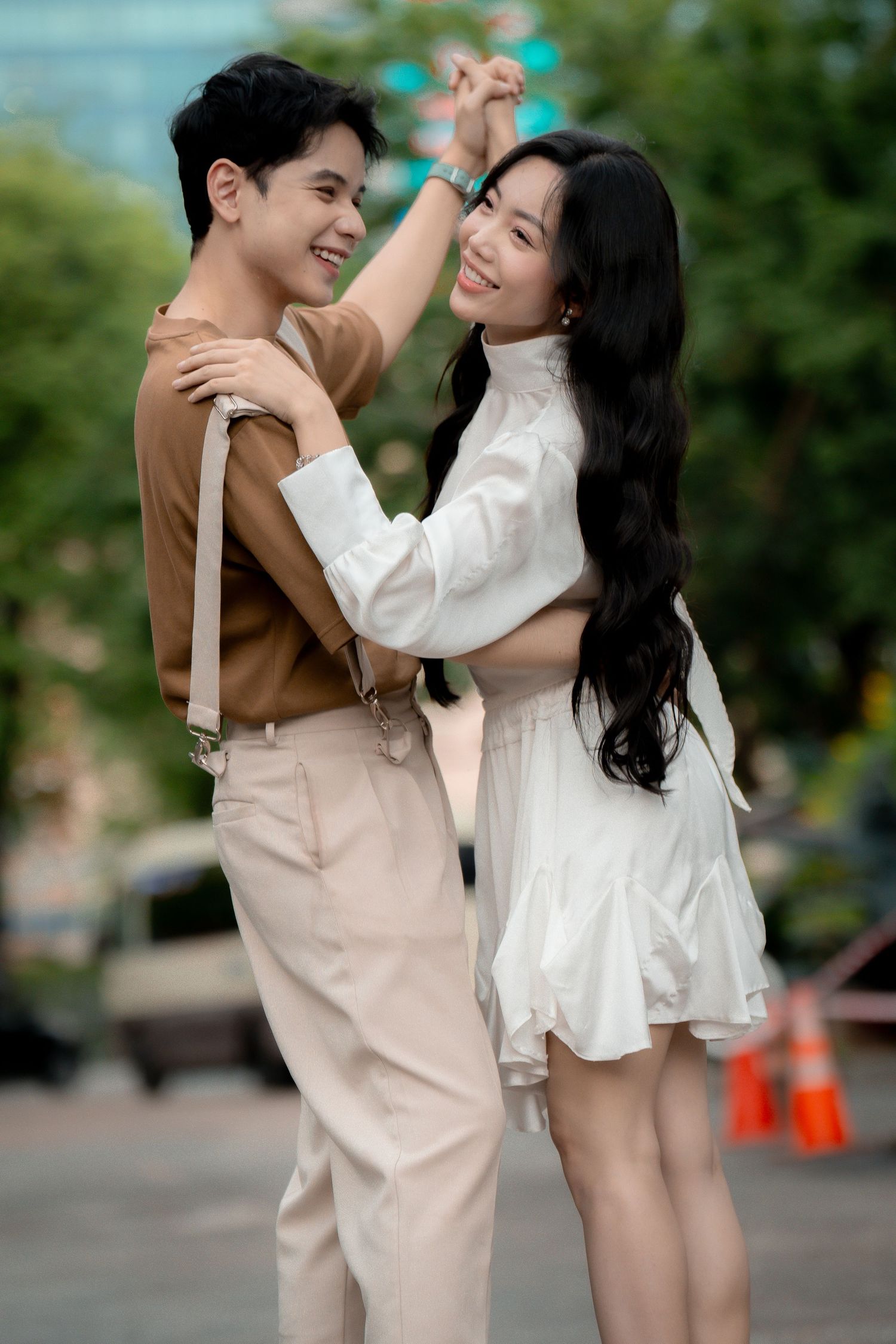Playful couple in brown and white outfits dancing outdoors.