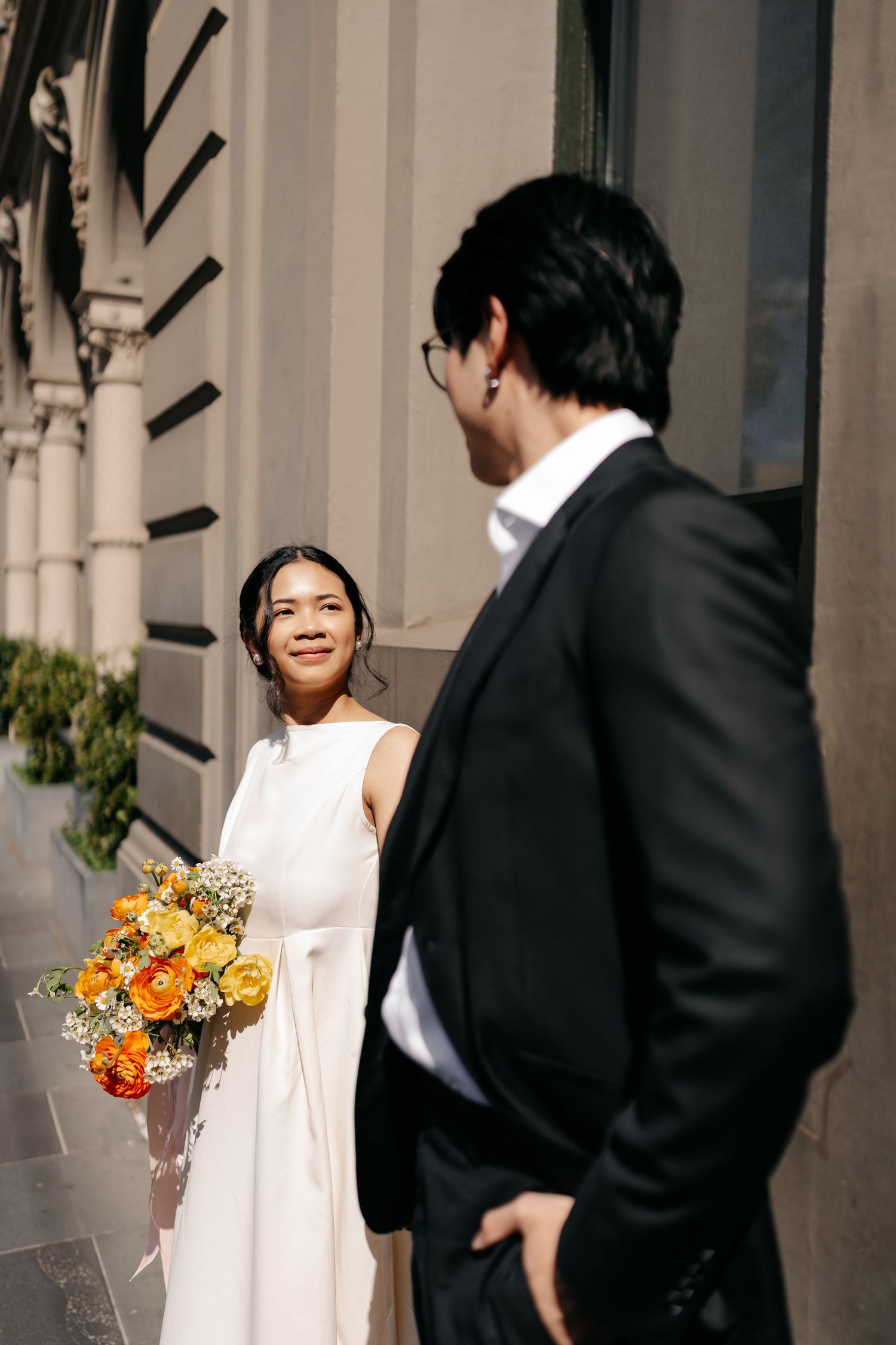 Elegant wedding couple interacts playfully in front of classic architectural columns.