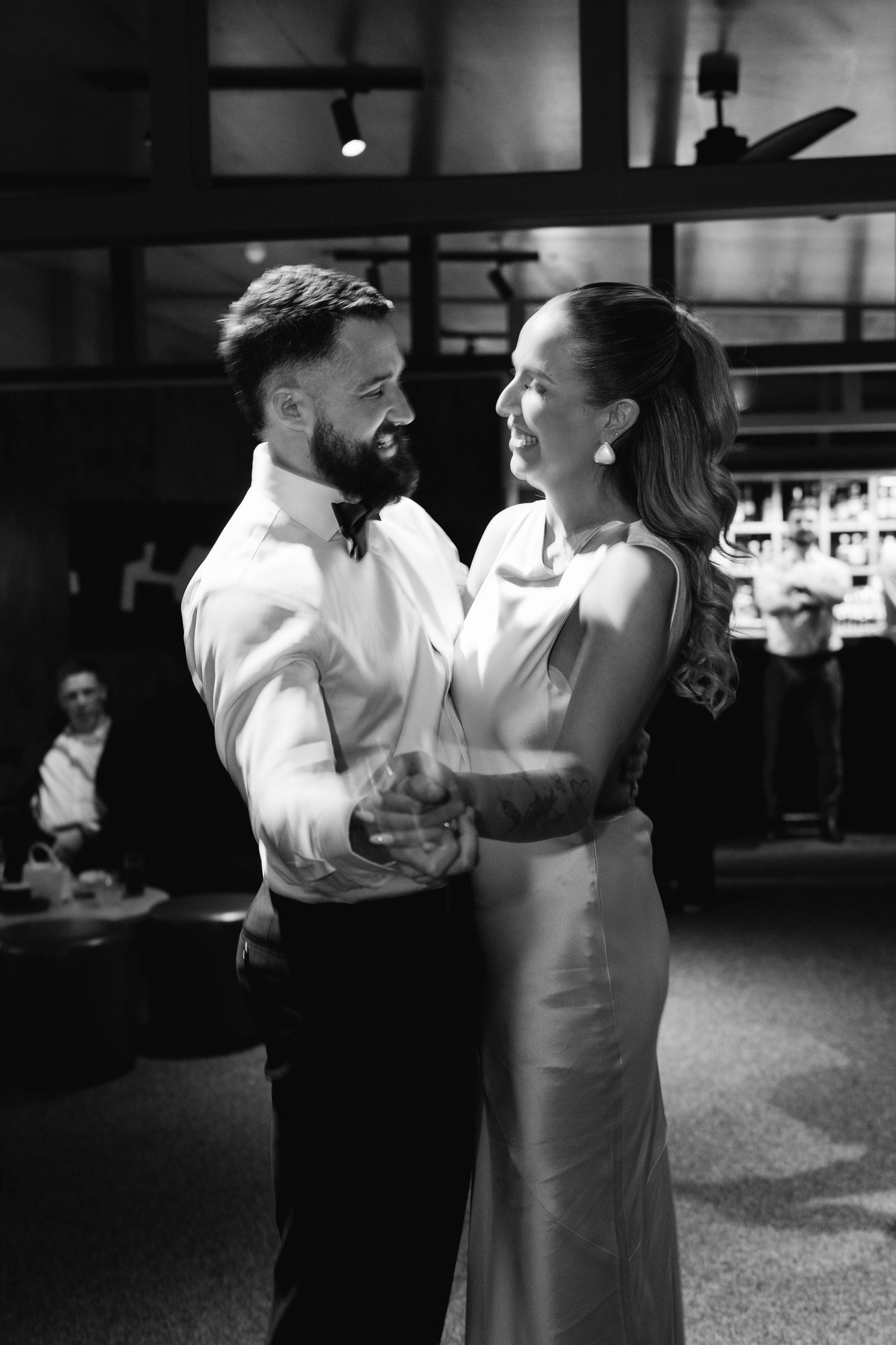 Couple dancing in formal attire at an elegant indoor venue in black and white.