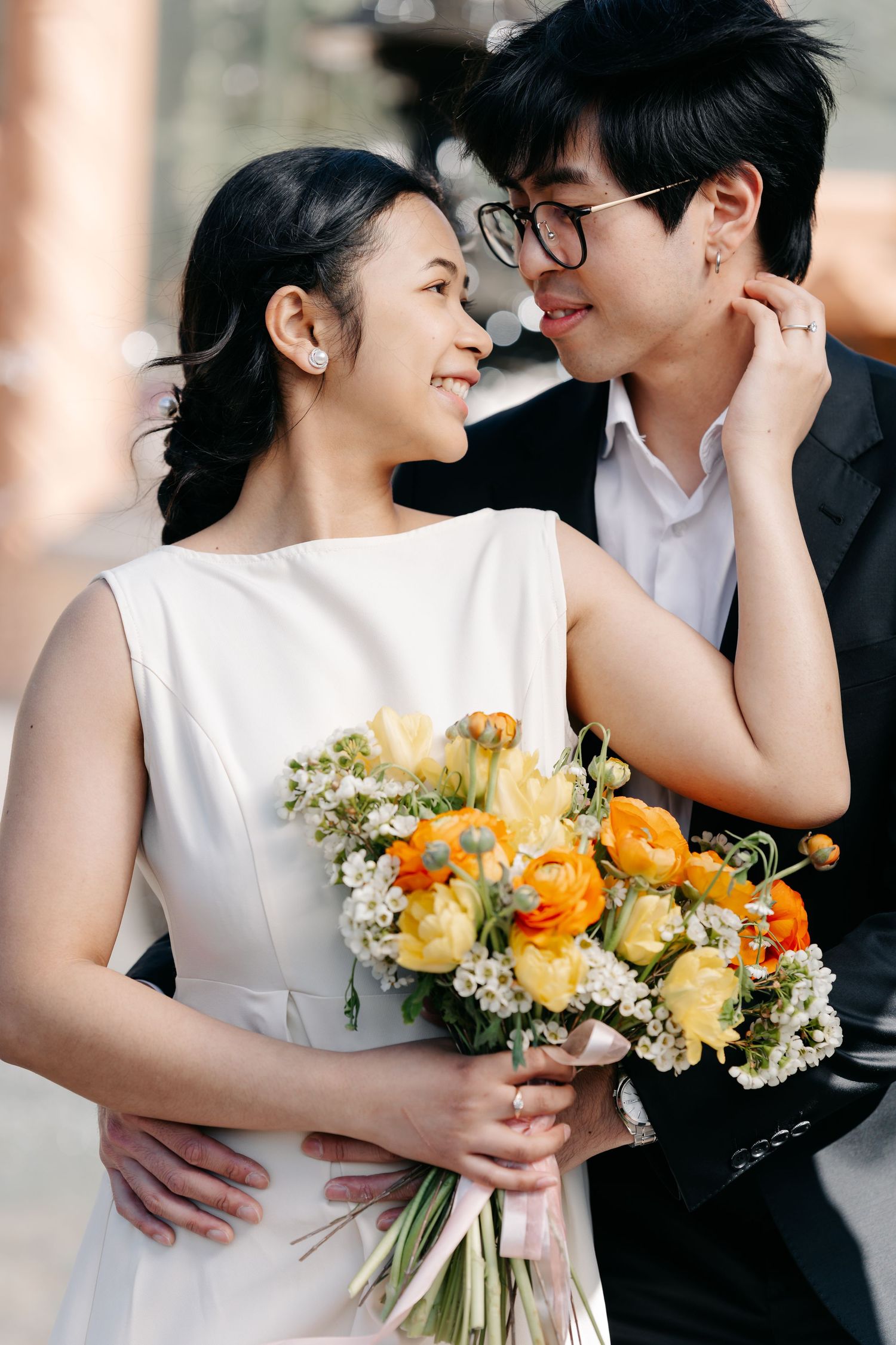 Joyful couple shares intimate moment with bride holding vibrant yellow and orange bouquet.