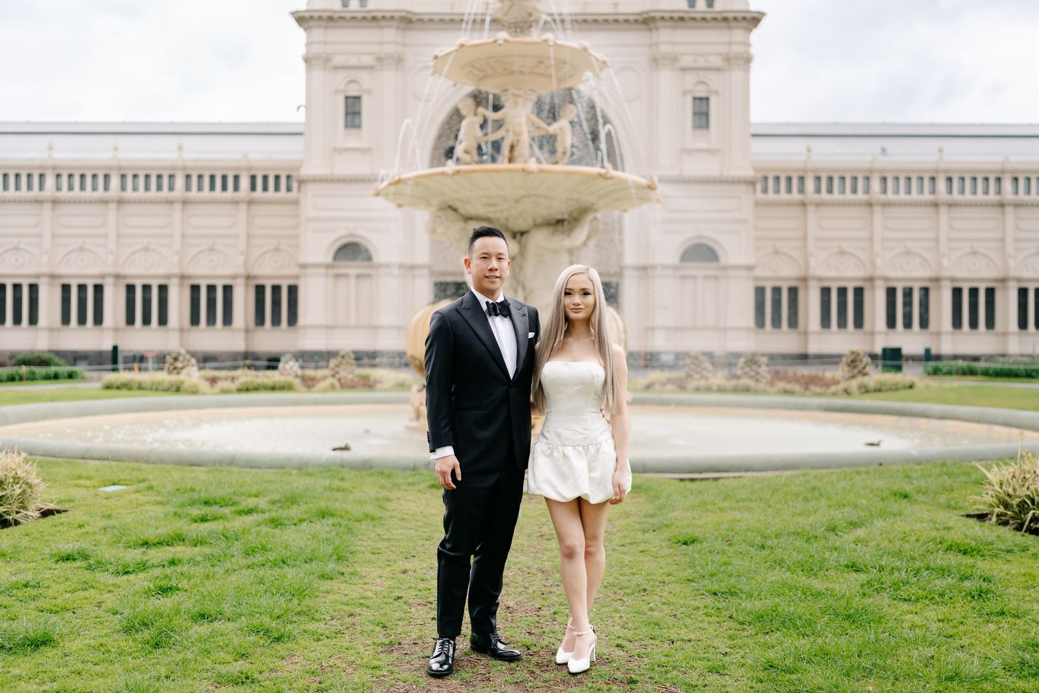 Couple walking on grass in front of grand historic building.