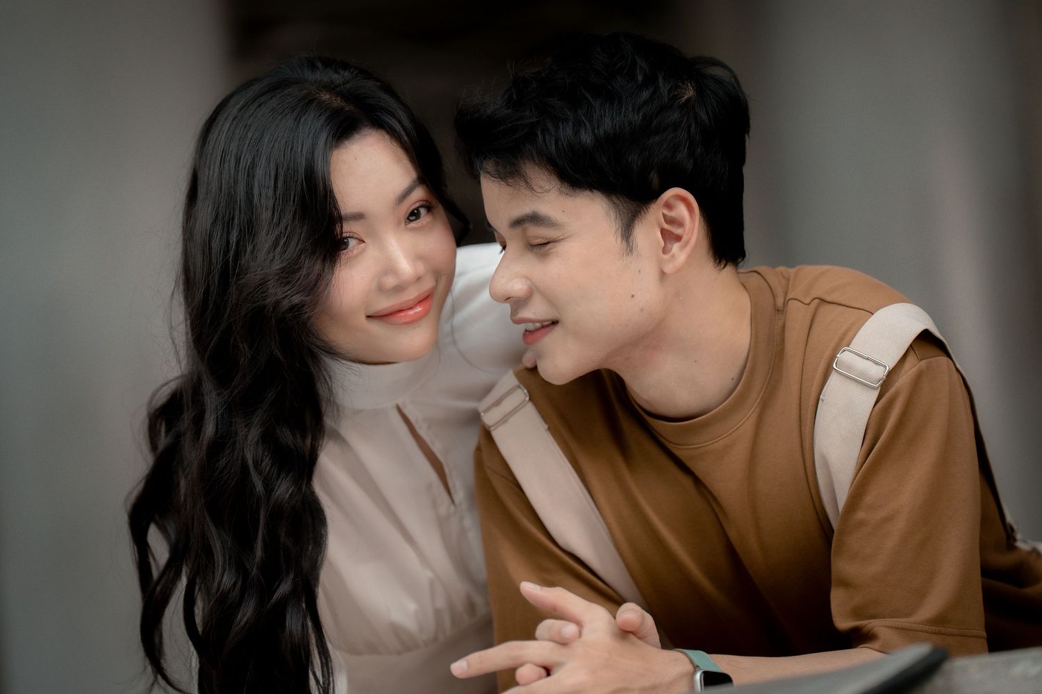 A couple shares tender moments together in matching neutral tones against a dark background.