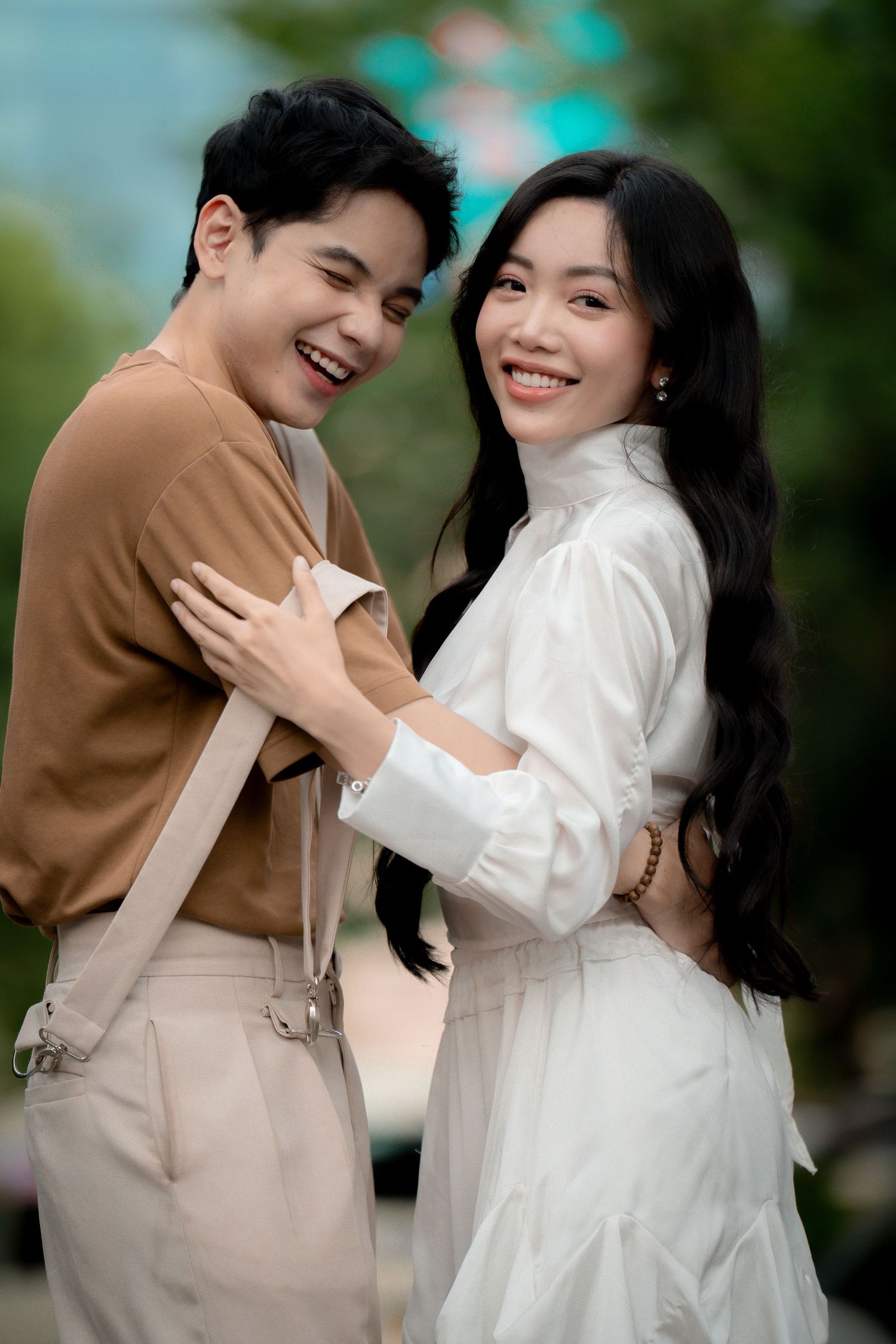 A joyful couple shares intimate moments while wearing coordinated brown and white outfits outdoors.