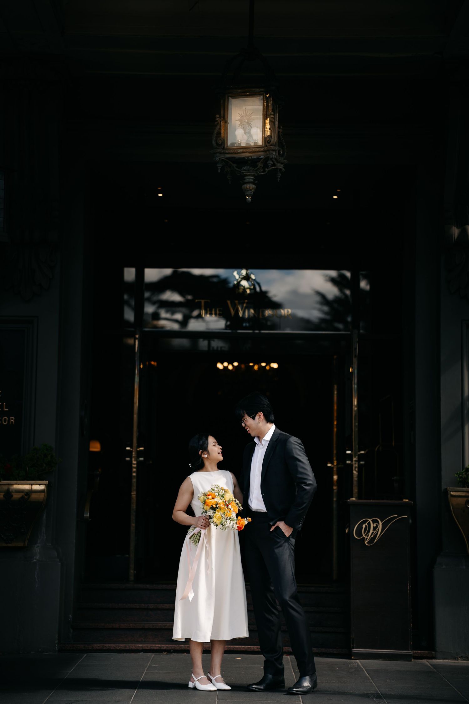 A romantic couple in wedding attire poses beneath an elegant lantern at a venue entrance.