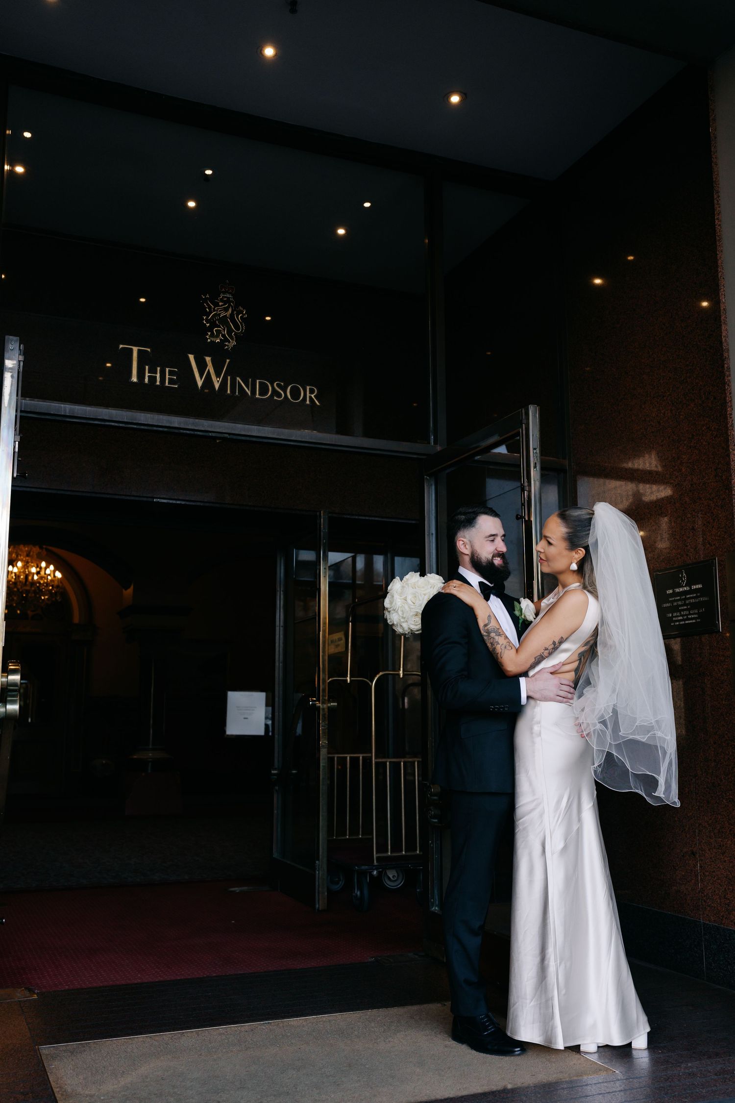 Elegant couple embracing outside The Windsor hotel entrance on their wedding day.