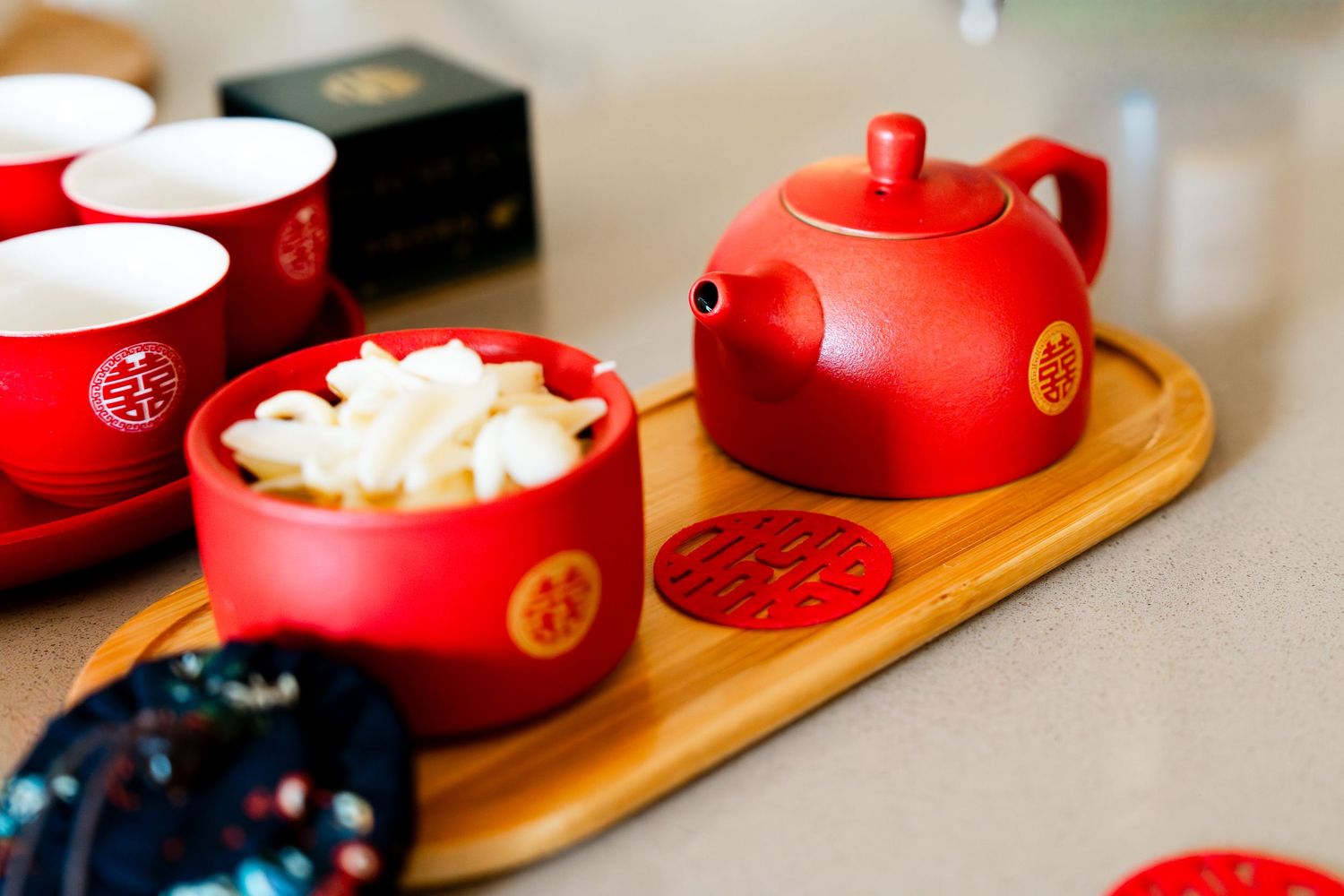 Red Chinese tea set with teapot and cups on bamboo tray, featuring traditional gold double happiness symbols.