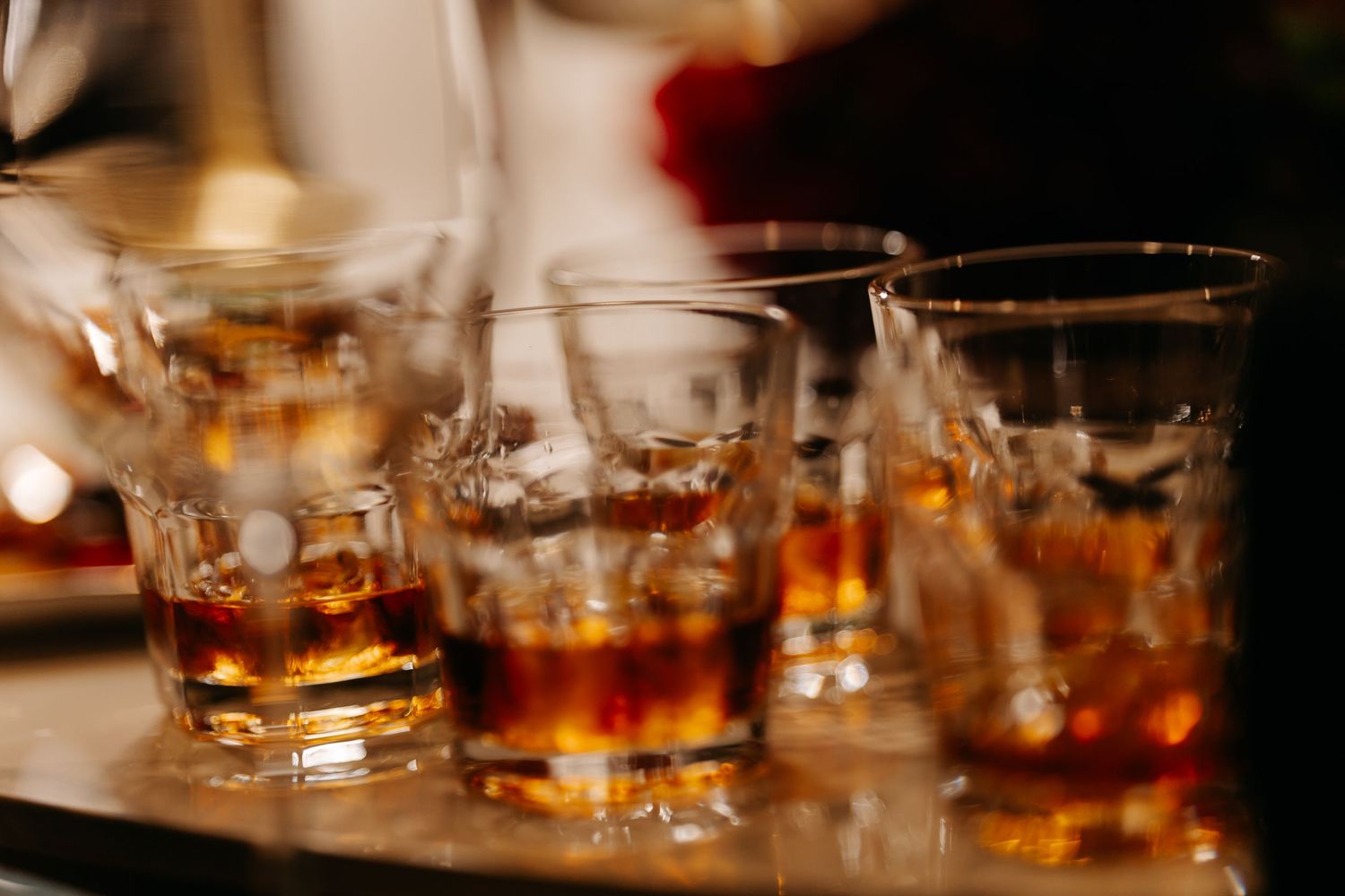 Several crystal whiskey glasses filled with amber bourbon whiskey served on a reflective tray at a bar.