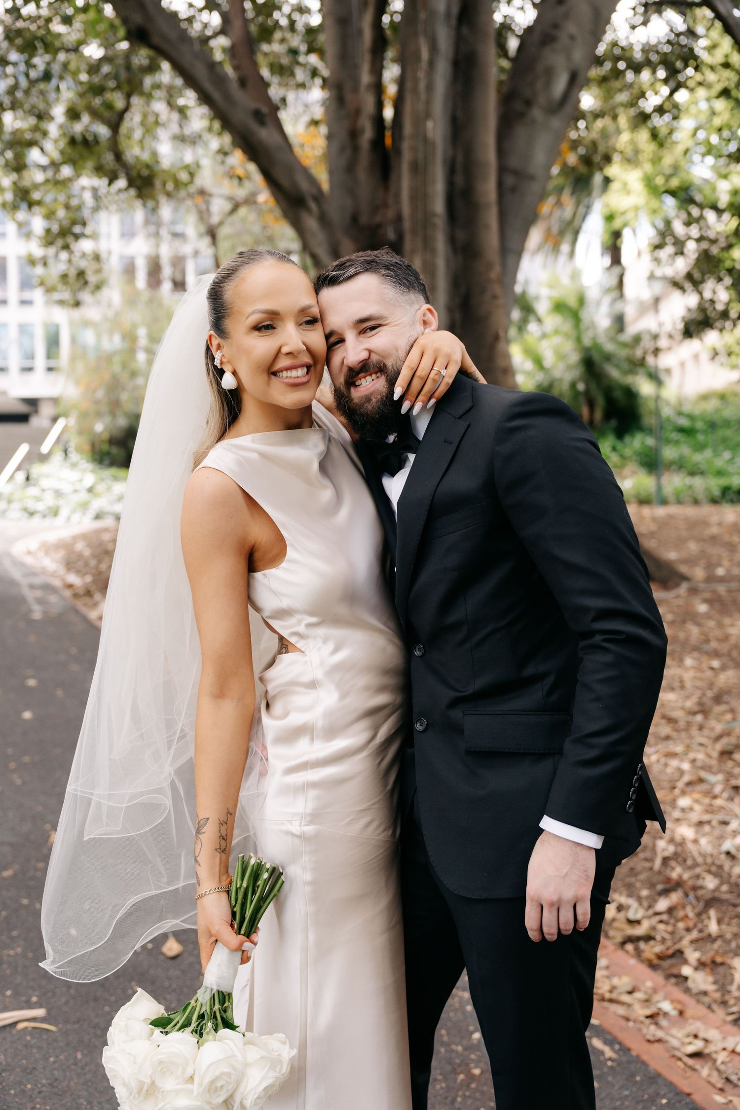 A happy couple shares joyful moments in their wedding attire under trees.