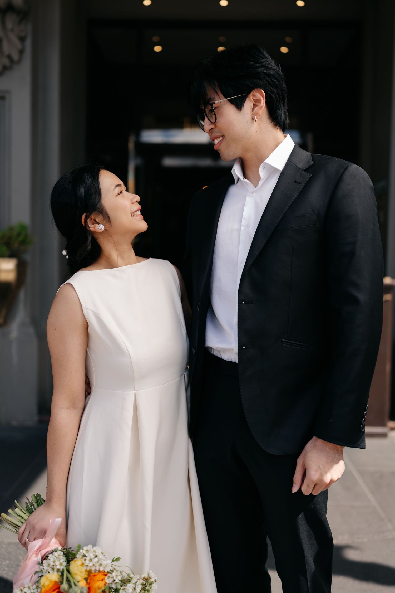 Wedding couple shares joyful moment together in elegant white dress and black suit with colorful bouquet.