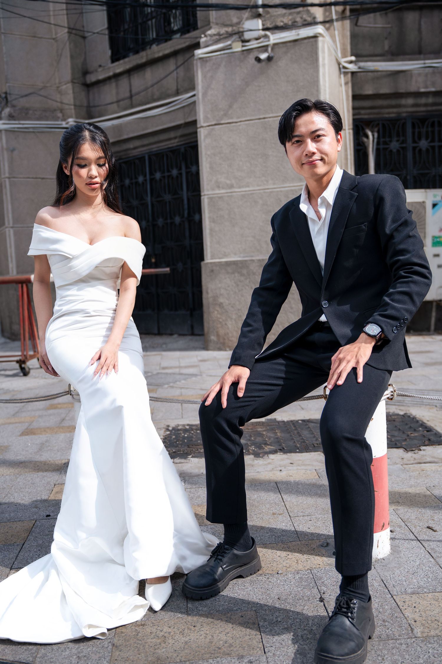 Wedding couple in contrasting white gown and black suit posing on urban street.