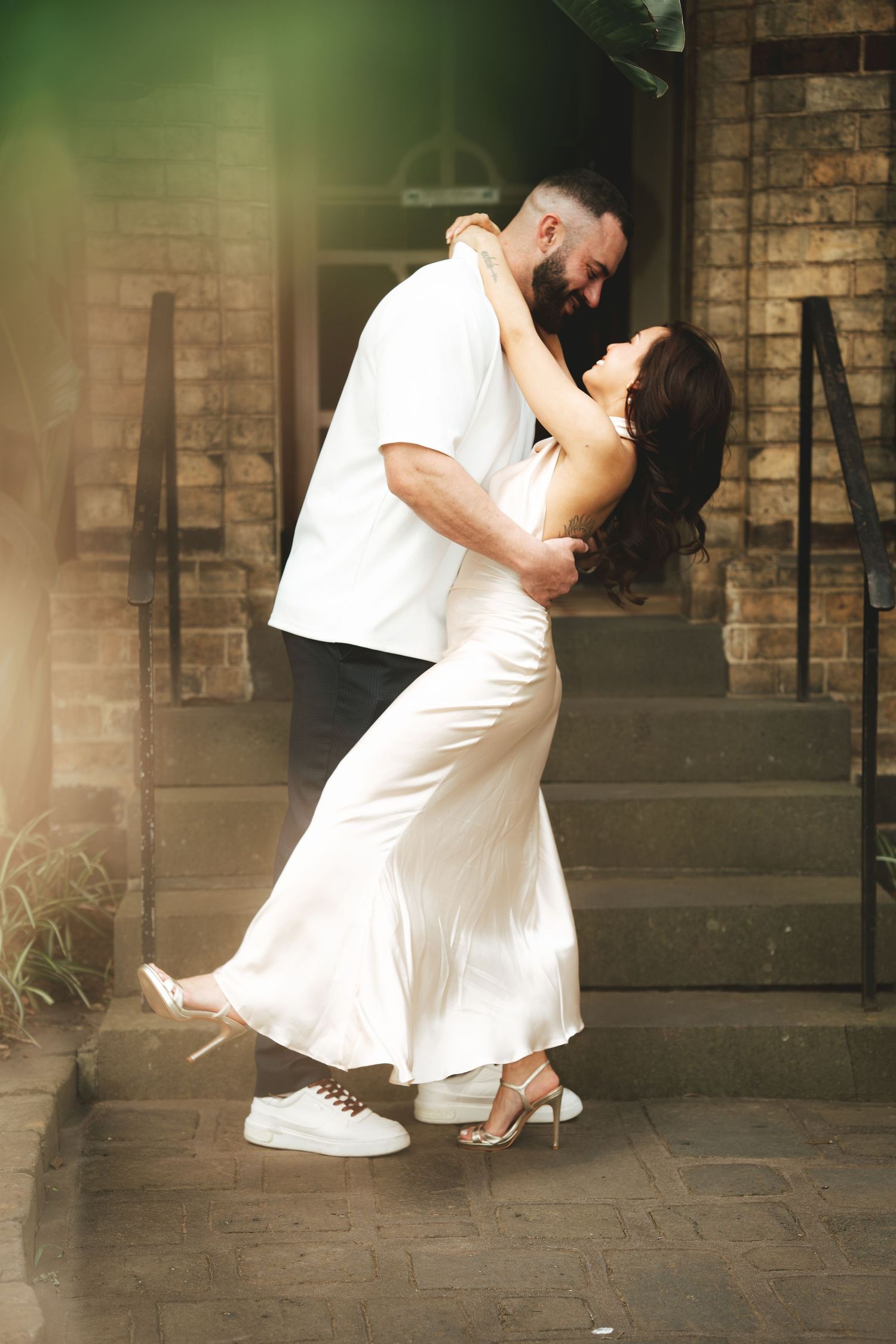 A romantic couple in white outfits dances together on a stone patio in a series of graceful dance poses.