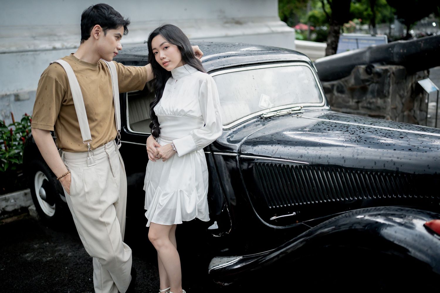Couple posing near vintage black car during romantic photoshoot.