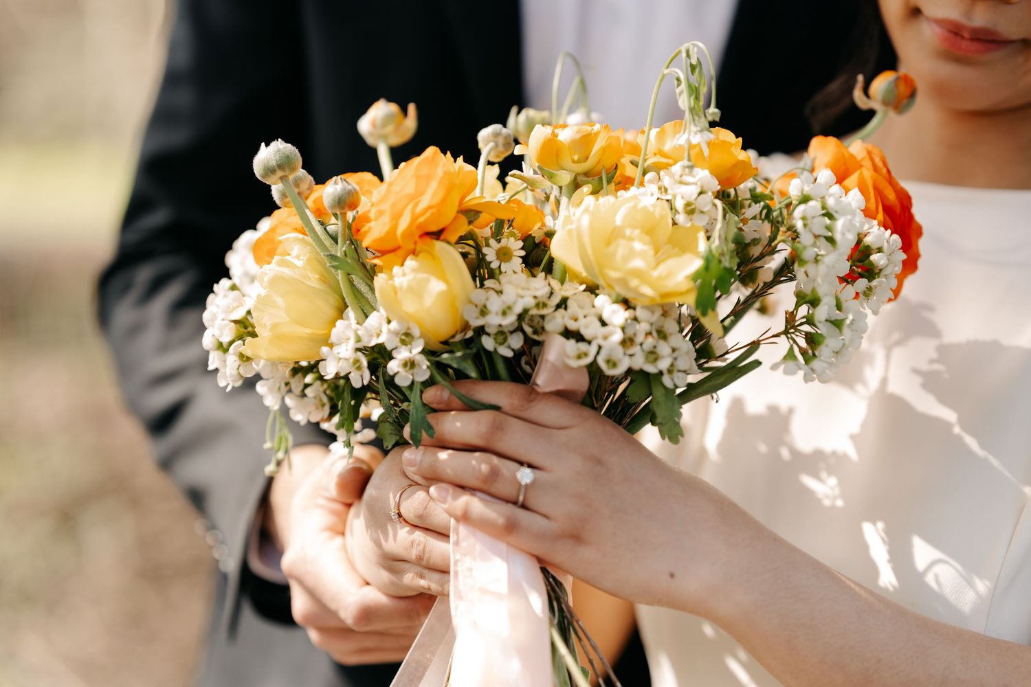 Detail shot of hands holding a beautiful orange and yellow floral bouquet.