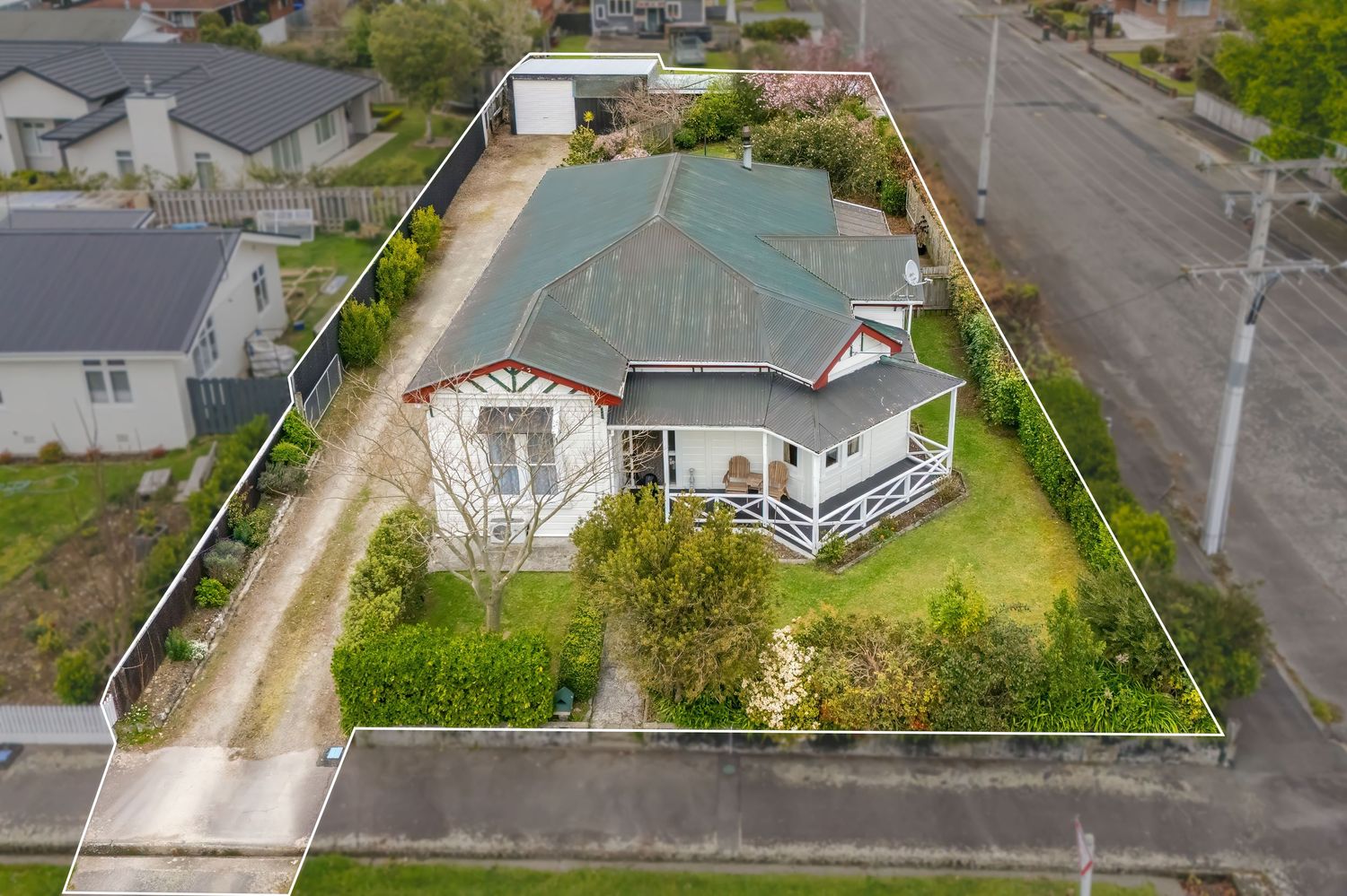 Aerial view of a charming weatherboard home with green roof, wraparound porch, large corner lot, and driveway in a residential suburb.