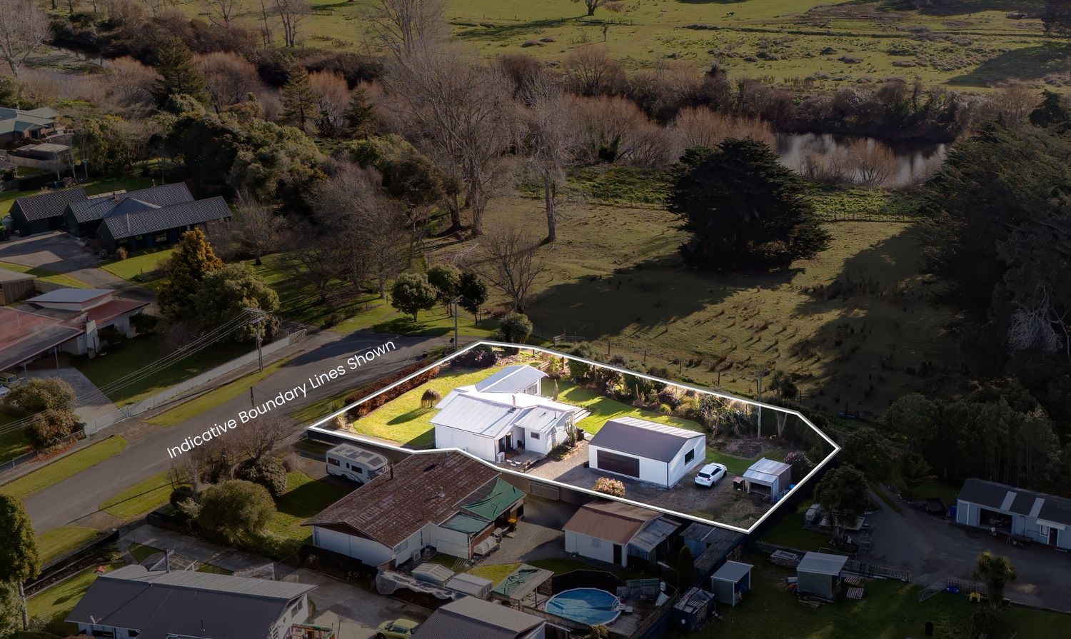 Aerial view of a residential property with a white house, large yard, and surrounding greenery in a quiet suburban neighborhood.